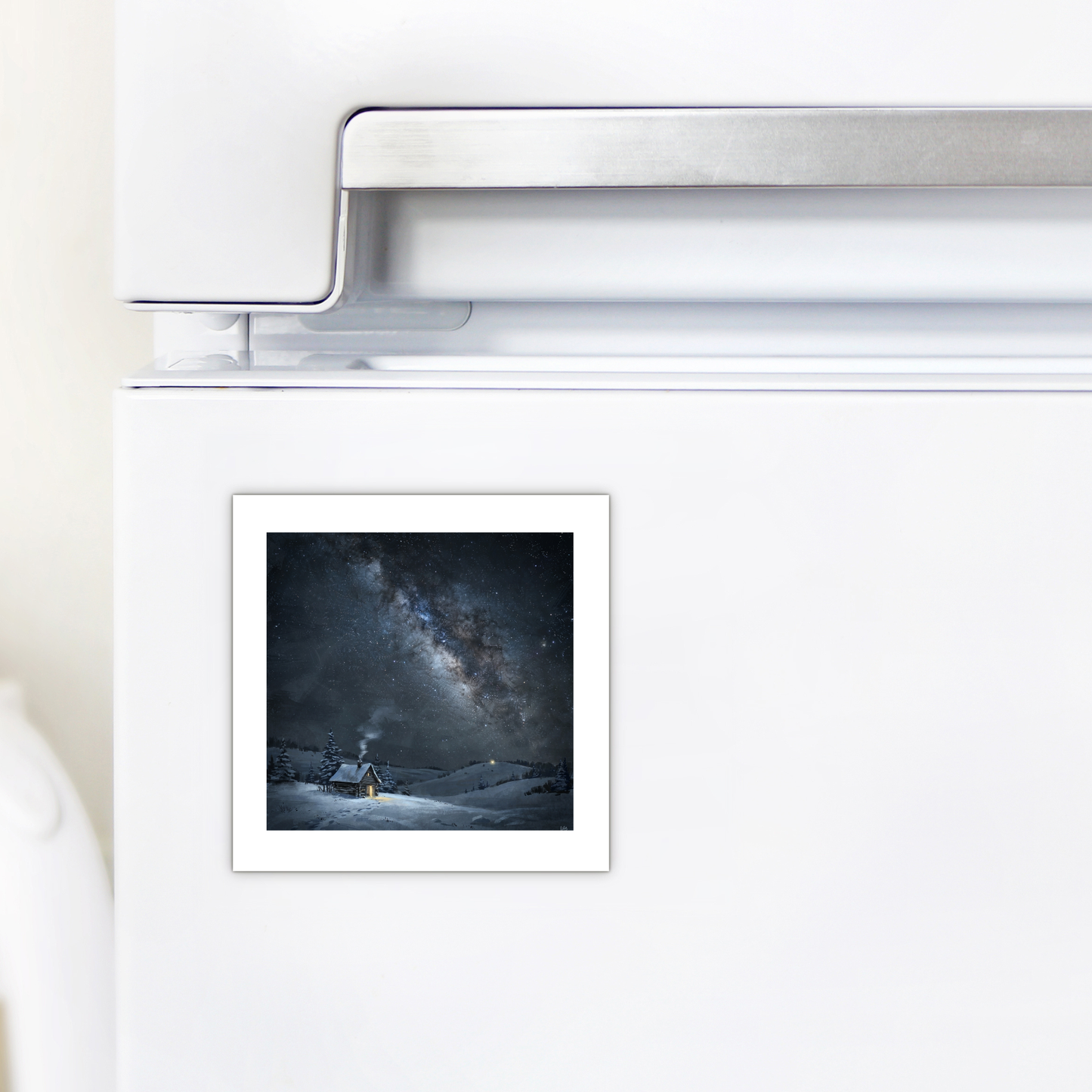 A small “The Night Is Listening Milky Way Magnet | Celestial Art” by Mirabilia Boutique, depicting a snowy landscape, a glowing tent, and a starry night sky, is attached to a white refrigerator door.