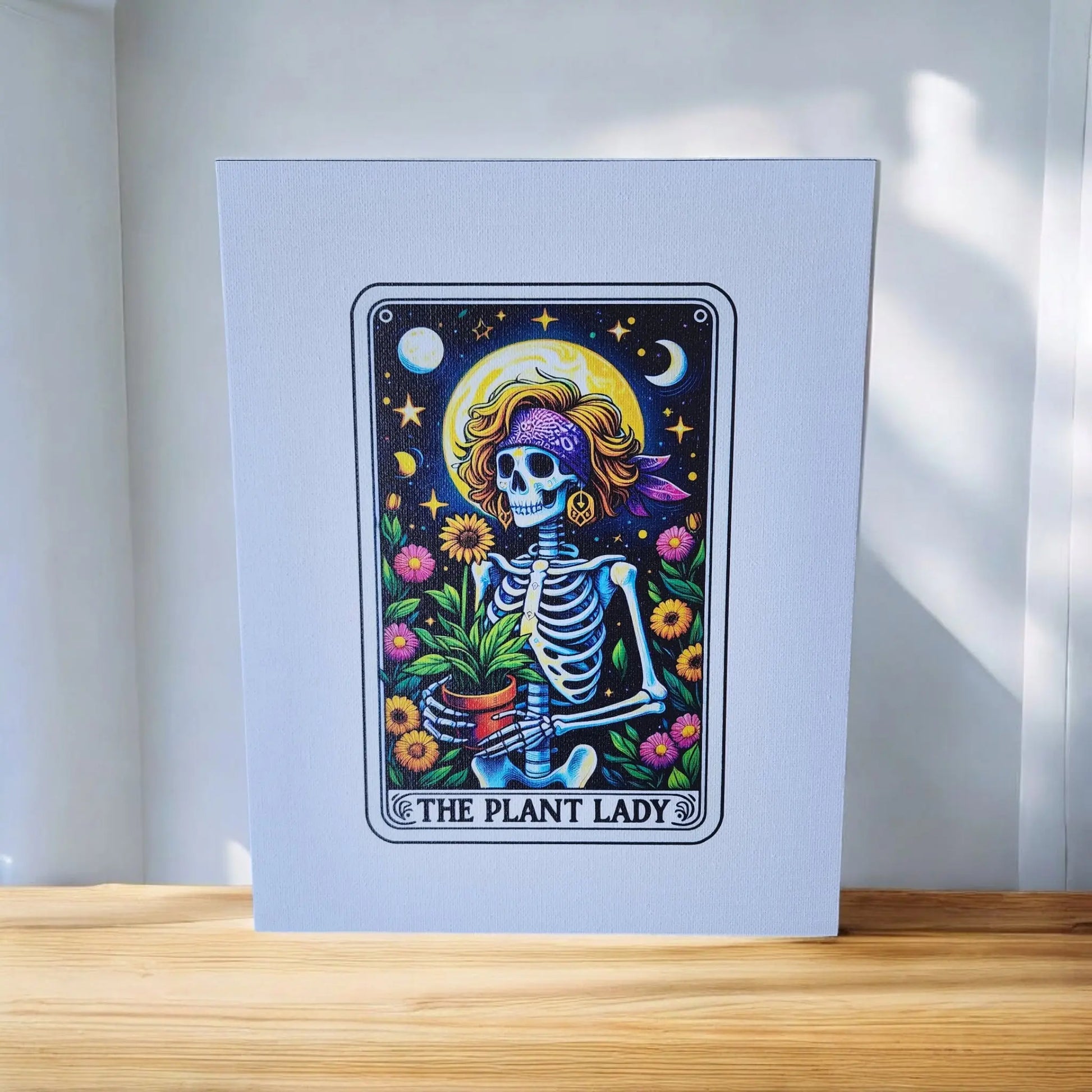 The Mirabilia Boutique's "The Plant Lady Gardening 8x10 Canvas Sign" features a whimsical skeleton wearing a purple headscarf and adorned with flowers, holding a potted plant. Stars, moons, and more flowers surround the skeleton against a dark background. Perfect for tarot lovers, the canvas includes the caption "THE PLANT LADY" at the bottom.