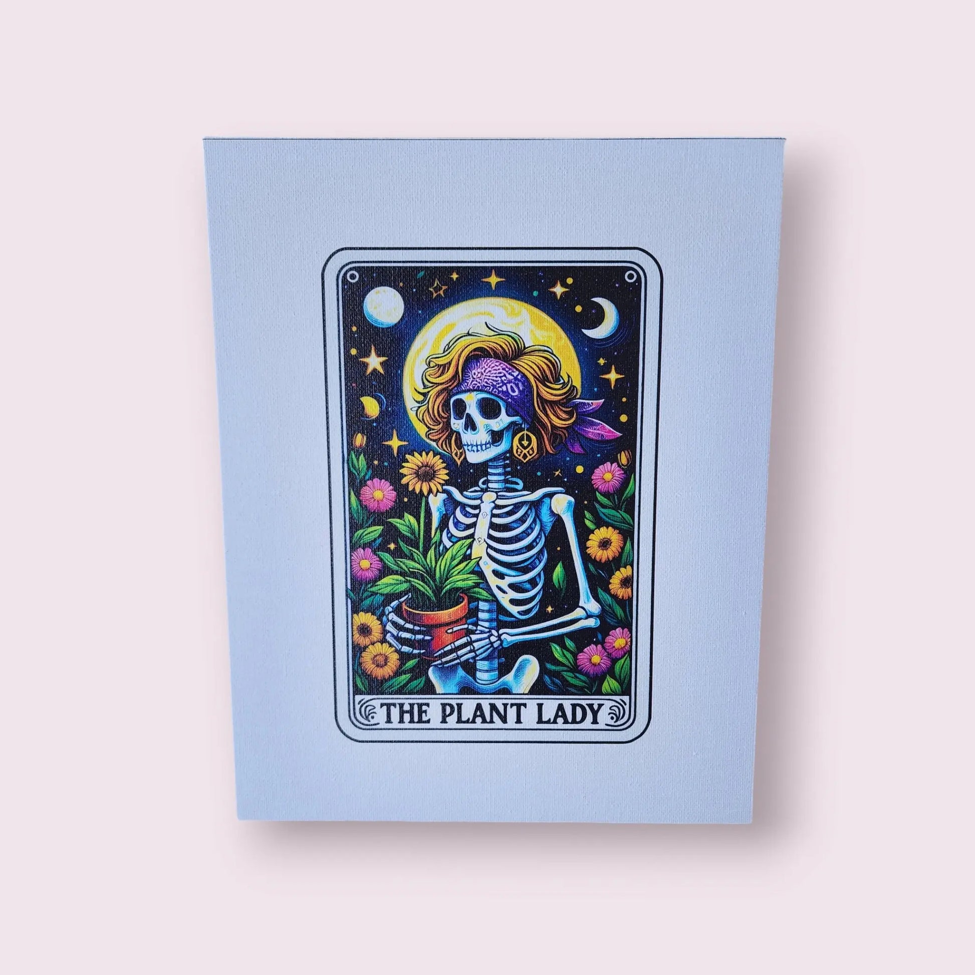 The "Plant Lady Gardening 8x10 Canvas Sign" by Mirabilia Boutique showcases a whimsical skeleton woman adorned with a purple headscarf and a golden halo, holding a potted plant. She is surrounded by vibrant flowers, stars, crescent moons, and a sun in tarot card style, all set against a light pink background. Ideal for collectors of Plant Lady Canvas artwork and tarot enthusiasts alike.