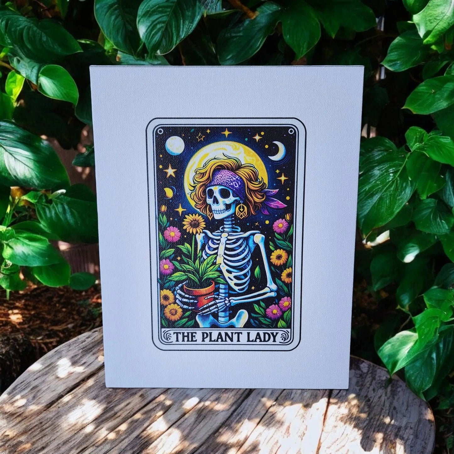 Introducing "The Plant Lady Gardening 8x10 Canvas Sign" by Mirabilia Boutique: a lively canvas print showcasing a whimsical skeleton adorned with a headscarf and sunglasses, clutching a potted plant. The backdrop captures a serene night sky with stars and moon, encircled by vibrant flowers. The phrase "THE PLANT LADY" is elegantly inscribed at the bottom—ideal for tarot enthusiasts in search of distinctive décor.