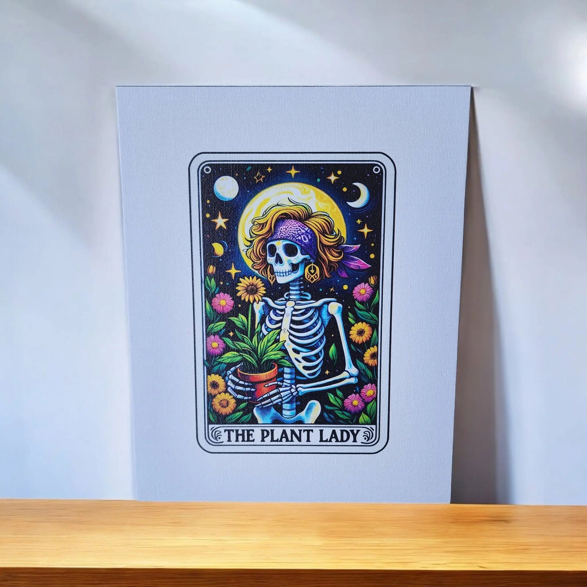 A vibrant illustration depicts a whimsical skeleton wearing a sunhat and a purple headband, holding a potted plant. The background showcases a night sky with stars and a crescent moon, surrounded by colorful flowers. The text at the bottom reads, "The Plant Lady Gardening 8x10 Canvas Sign." Brought to you by Mirabilia Boutique, this piece is perfect for tarot lovers.