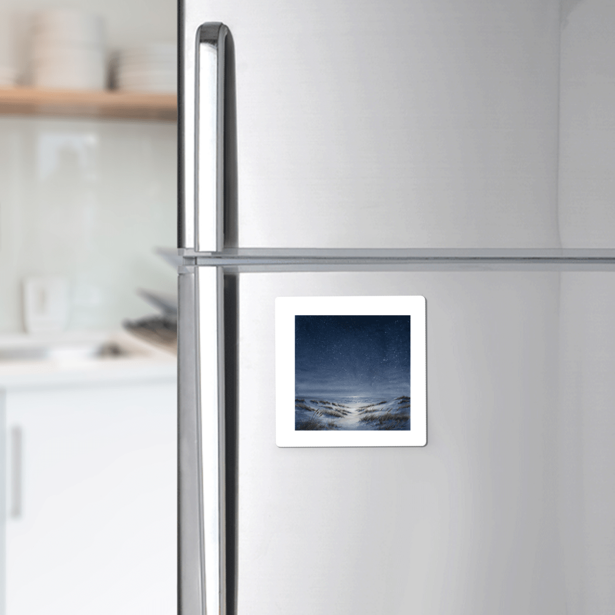 A stainless steel refrigerator with The Sea Keeps Its Own Stars Magnet from Mirabilia Boutique—featuring a snowy landscape and night sky—attached to the door; kitchen shelves and dishes are visible in the background.