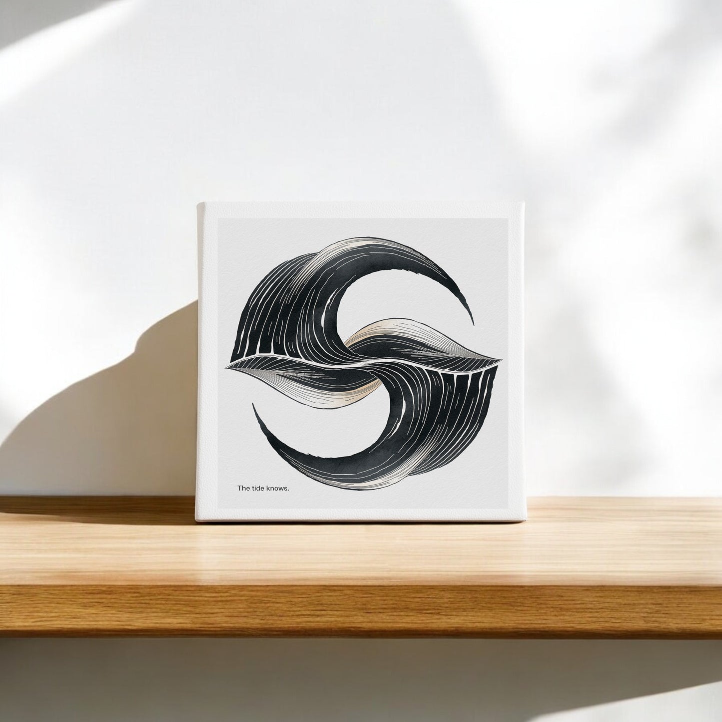 The Tide Knows Canvas – 8x8 Abstract Coastal Wall Art" by Mirabilia Boutique features black and gray swirling strokes in an "S" shape on canvas, sitting on a wooden shelf with soft shadows—perfect minimalist decor for any space.