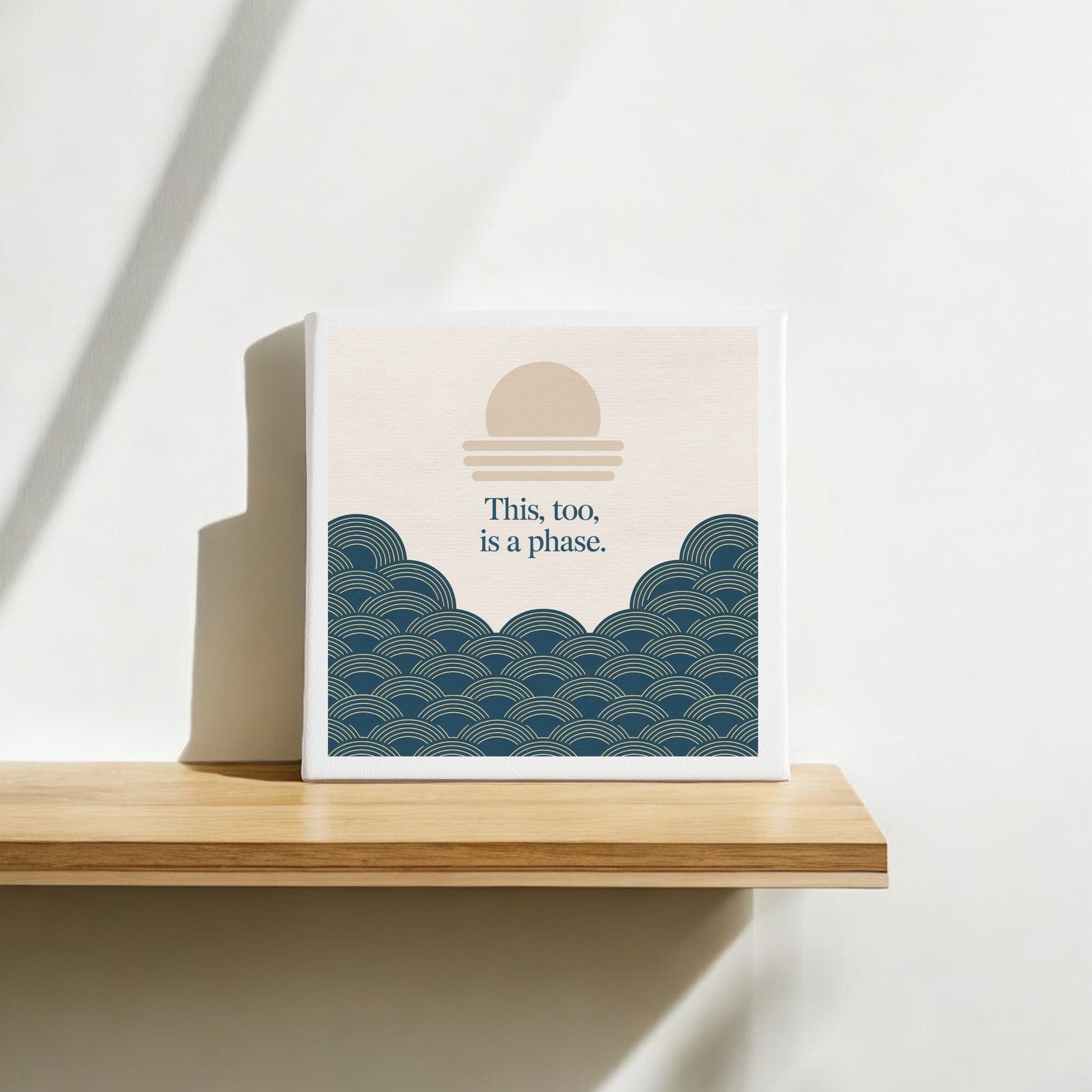 The This Too Is a Phase Canvas – Calming Summer Wall Art from Mirabilia Boutique features a minimalist sun and blue waves with the words “This, too, is a phase,” perfect for adding tranquil decor to your shelf or wall.