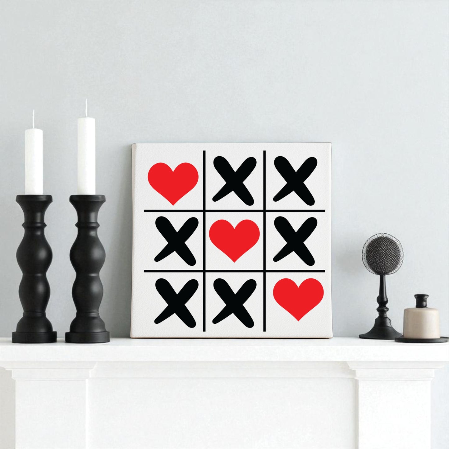 The Tic Tac Toe Love Sign 8x8 Valentine Canvas Wall Art by Mirabilia Boutique adds charming Valentine’s decor to the mantel, paired with black candlesticks, a round black microphone, and a small beige jar.