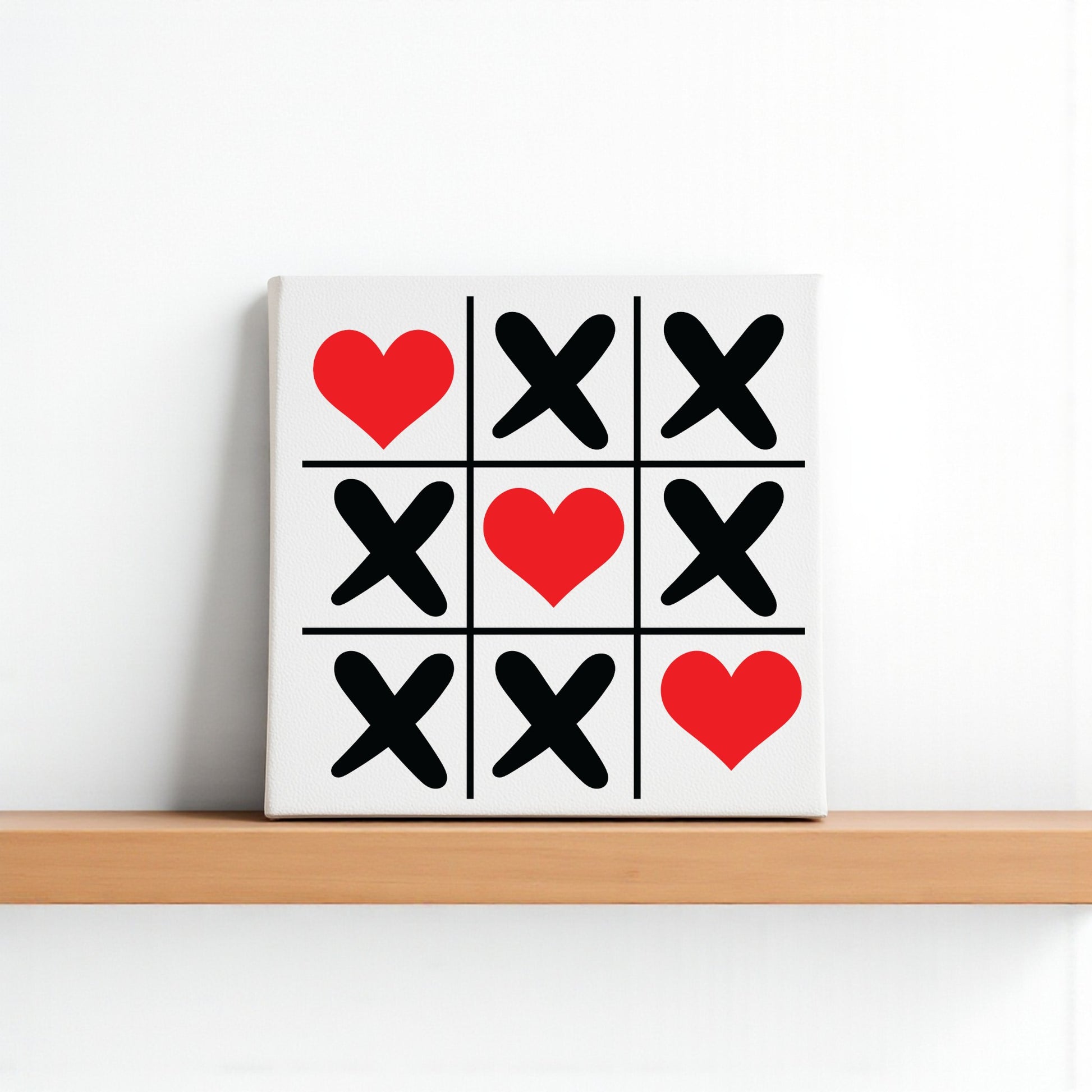 The Mirabilia Boutique 'Tic Tac Toe Love Sign' is an 8x8 Valentine canvas with red hearts in the top left, center, and bottom right squares, plus black X’s—ideal as heart wall art or Valentine’s Day decor for your shelf or wall.