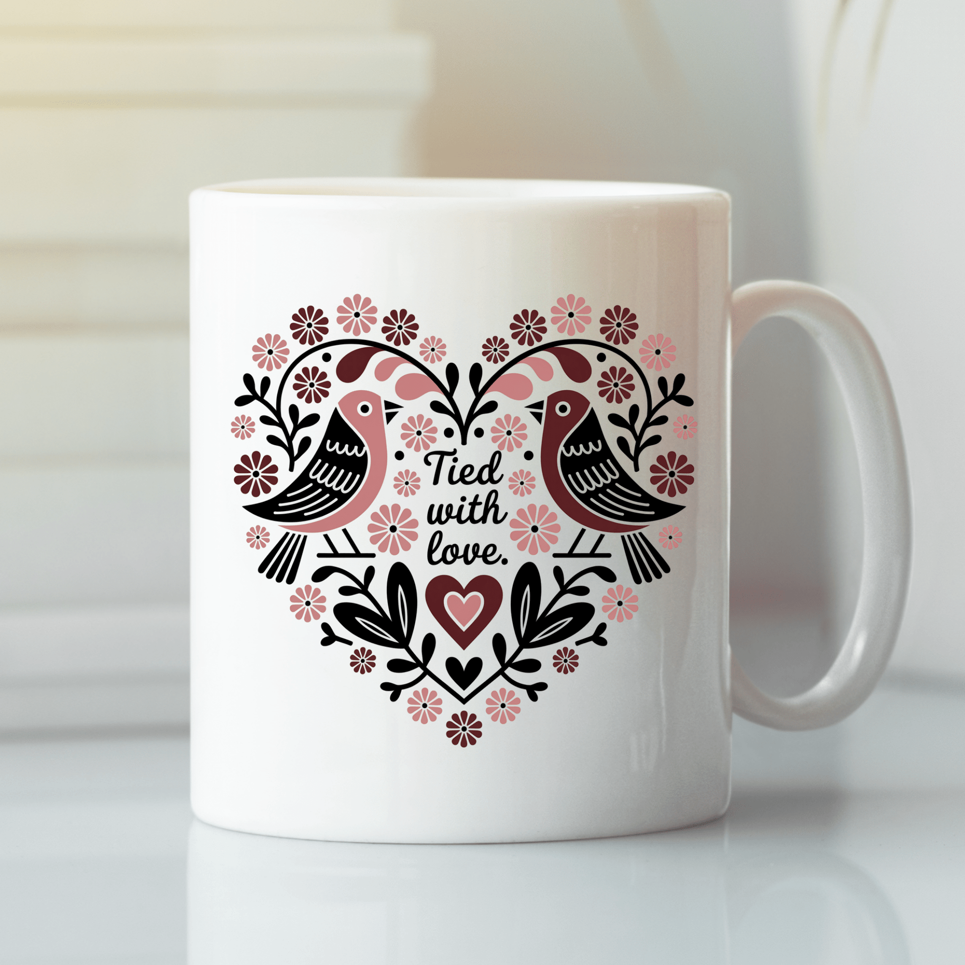 The Tied With Love Mug by Mirabilia Boutique features two white birds facing each other, a heart-shaped folk art floral motif, and the phrase "Tied with love"—a charming anniversary gift.
