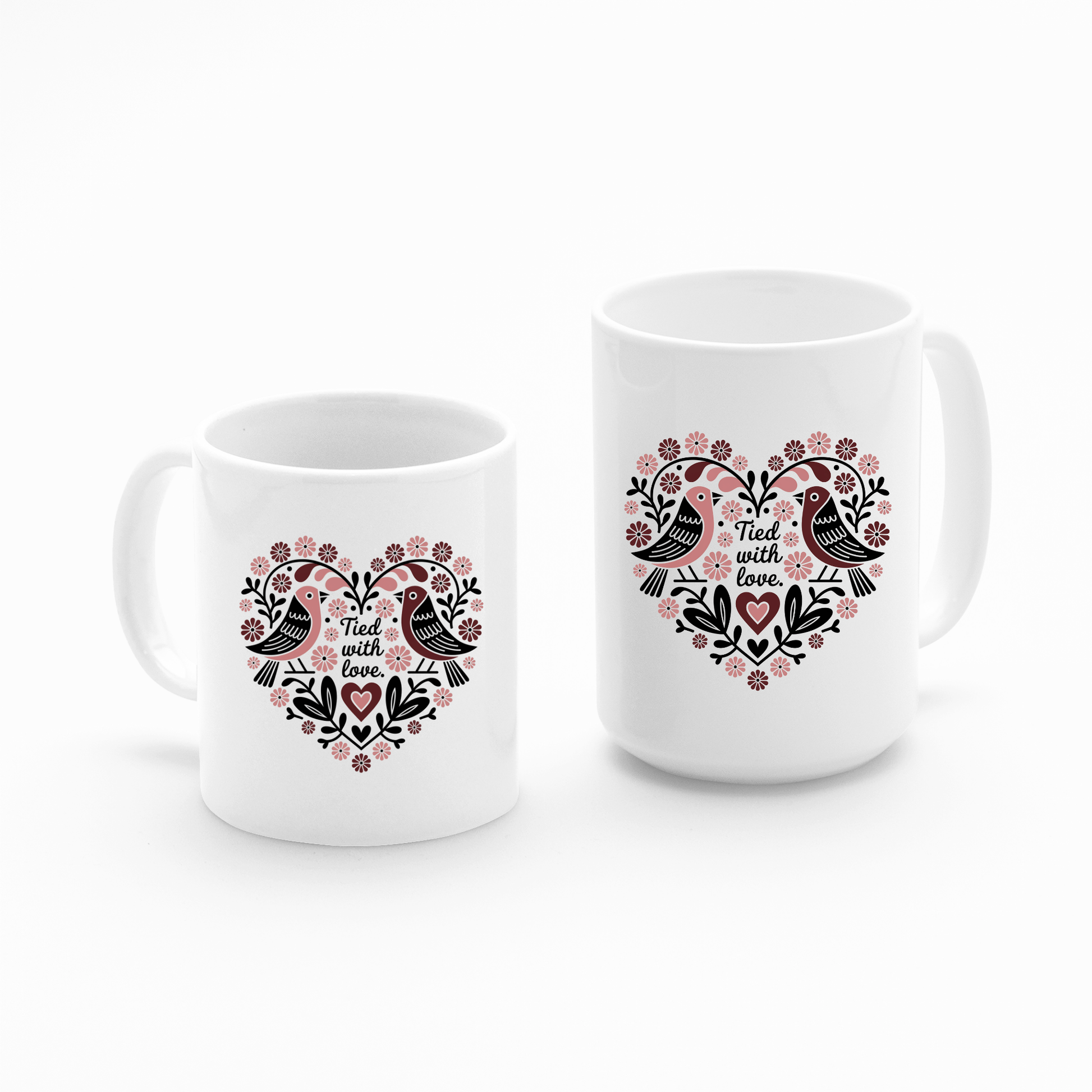 The Mirabilia Boutique "Tied With Love Mug – Folk Art Heart & Birds" set includes two white ceramic mugs (small and large), each with a heart-shaped floral design, two birds, and "Tied with love"—perfect for anniversaries or self-love.