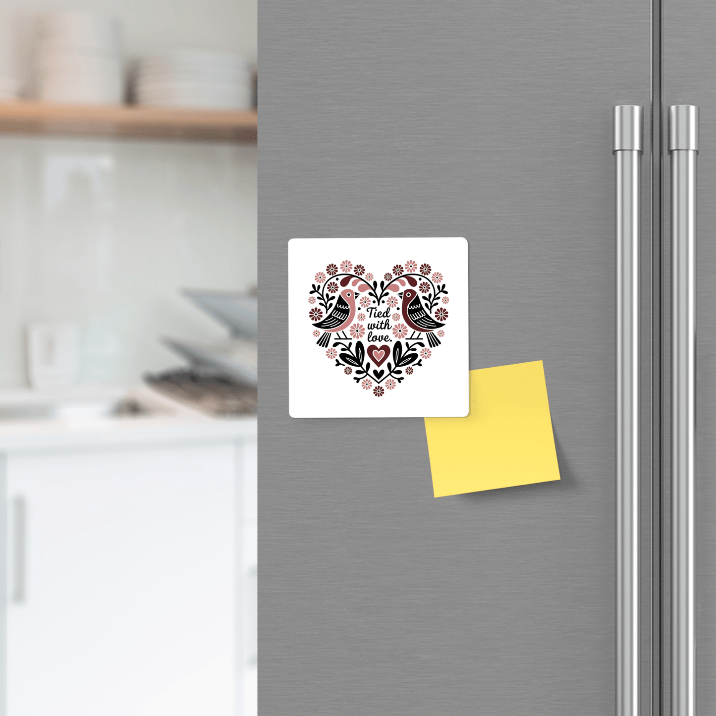 A silver refrigerator displays Mirabilia Boutique's "Tied With Love Birds Magnet" and a blank yellow sticky note. Kitchen shelves and dishes are visible in the background.