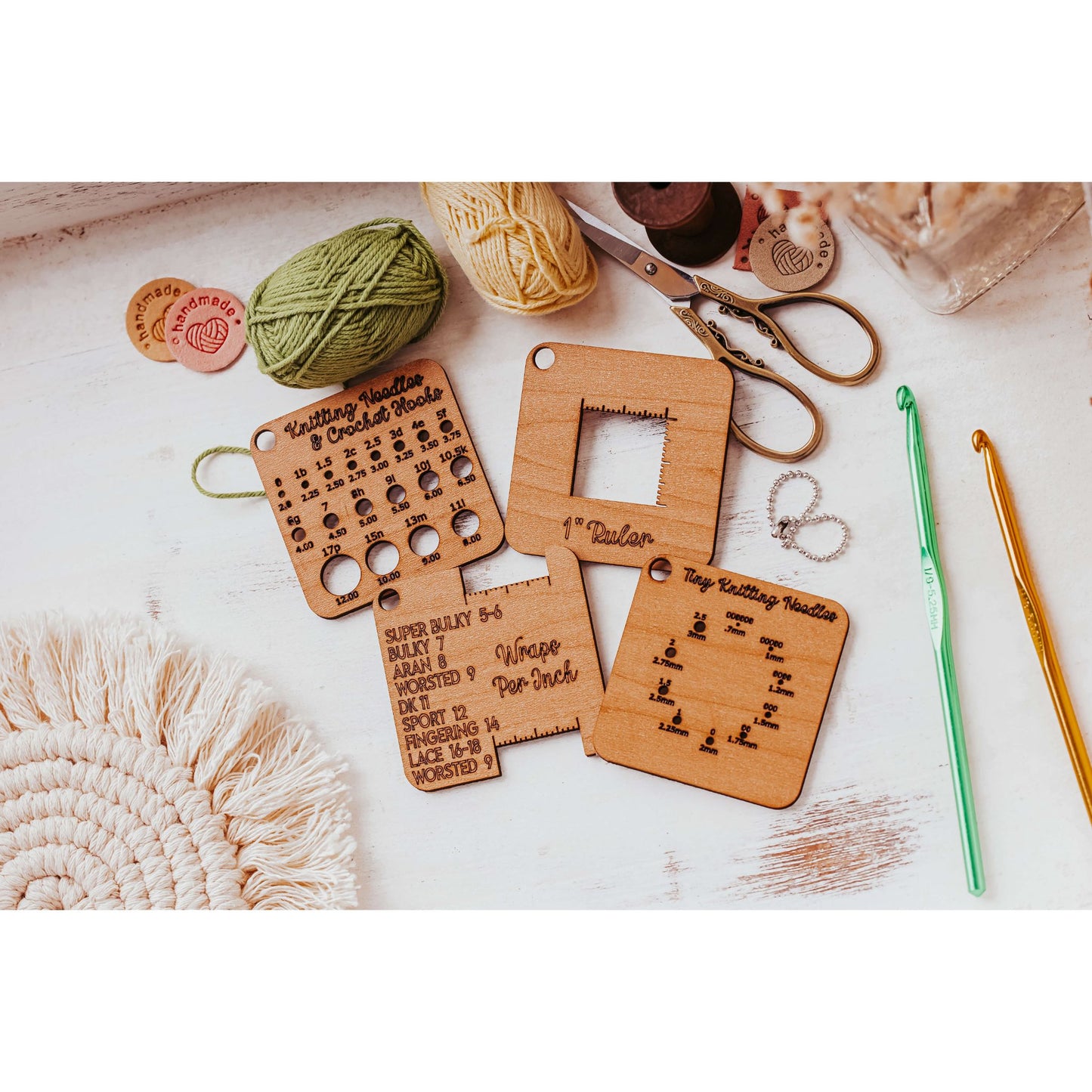 The Knitter’s Pocket Tool Set from Mirabilia Boutique, featuring 4 mini wooden tools with engraved measurement guides and stitch patterns, rests on a white surface surrounded by colorful yarn, knitting needles, scissors, and a woven placemat.