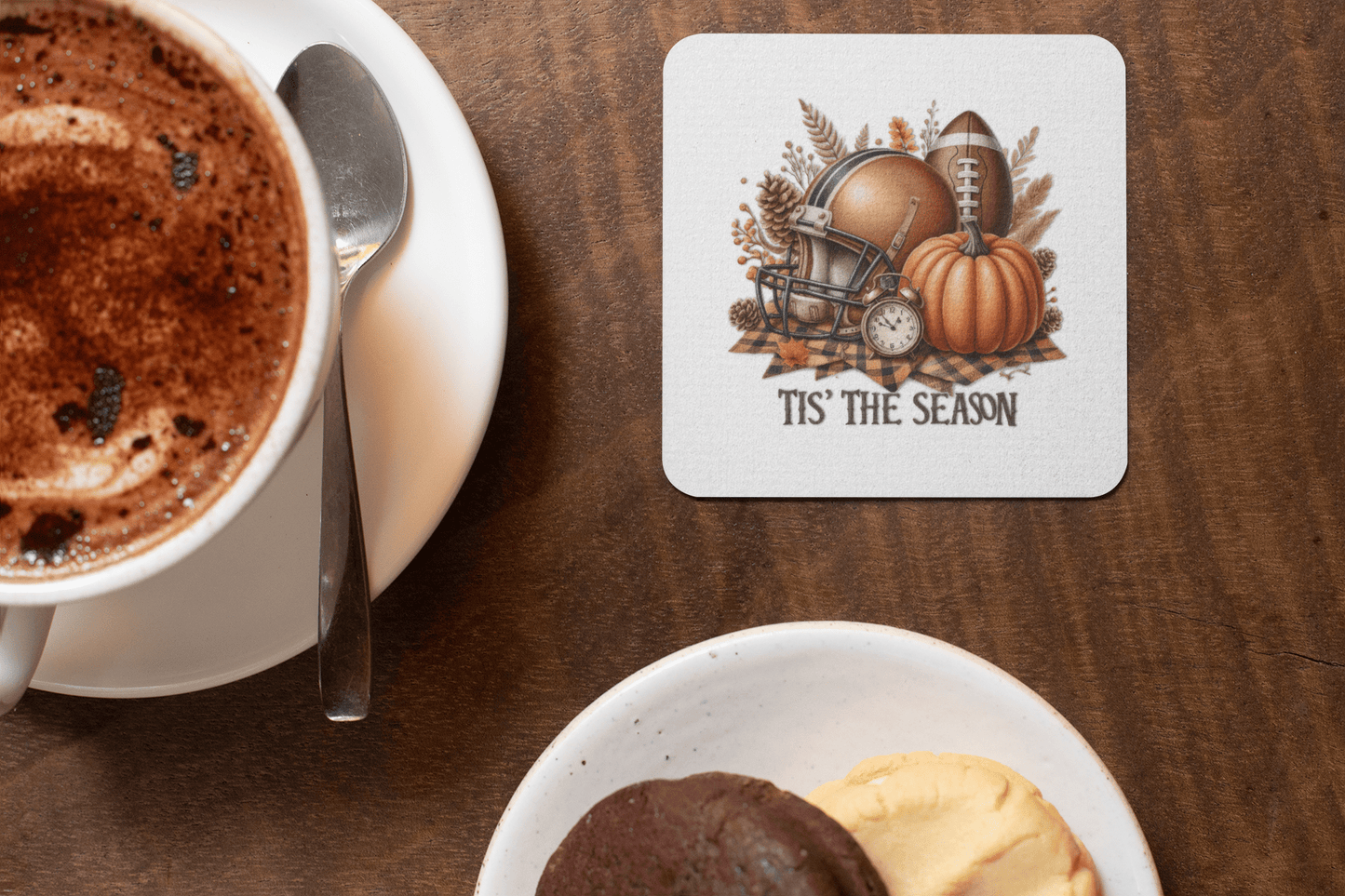 A cup of hot chocolate rests beside the Mirabilia Boutique “Tis’ the Season” Coaster Set—fall football pumpkin decor—while a plate with two cookies completes this cozy autumn scene.