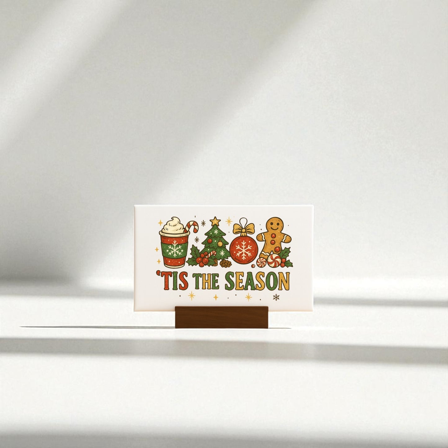The 'Tis the Season Mini Canvas from Mirabilia Boutique is a 6x4 Christmas sign on a wooden base featuring festive art—a hot drink, tree, ornament, gingerbread cookie, and bold yellow text—perfect for holiday gifts or cheerful decor.