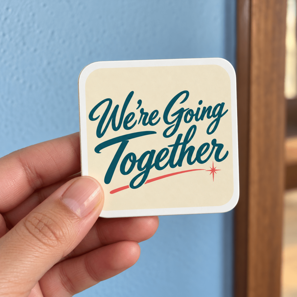 A hand holds a square We’re Going Together Magnet | Chrome & Starlight, featuring dark teal script and a small red star accent.