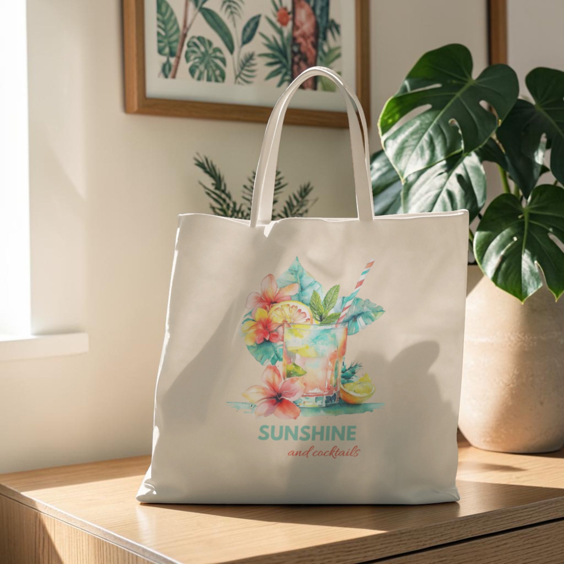 The Sunshine and Cocktails Canvas Tote Bag by Mirabilia Boutique, adorned with a colorful tropical drink and vibrant flowers design with the phrase "SUNSHINE and cocktails," rests on a wooden table beside a large leafy plant and sunlit framed art.