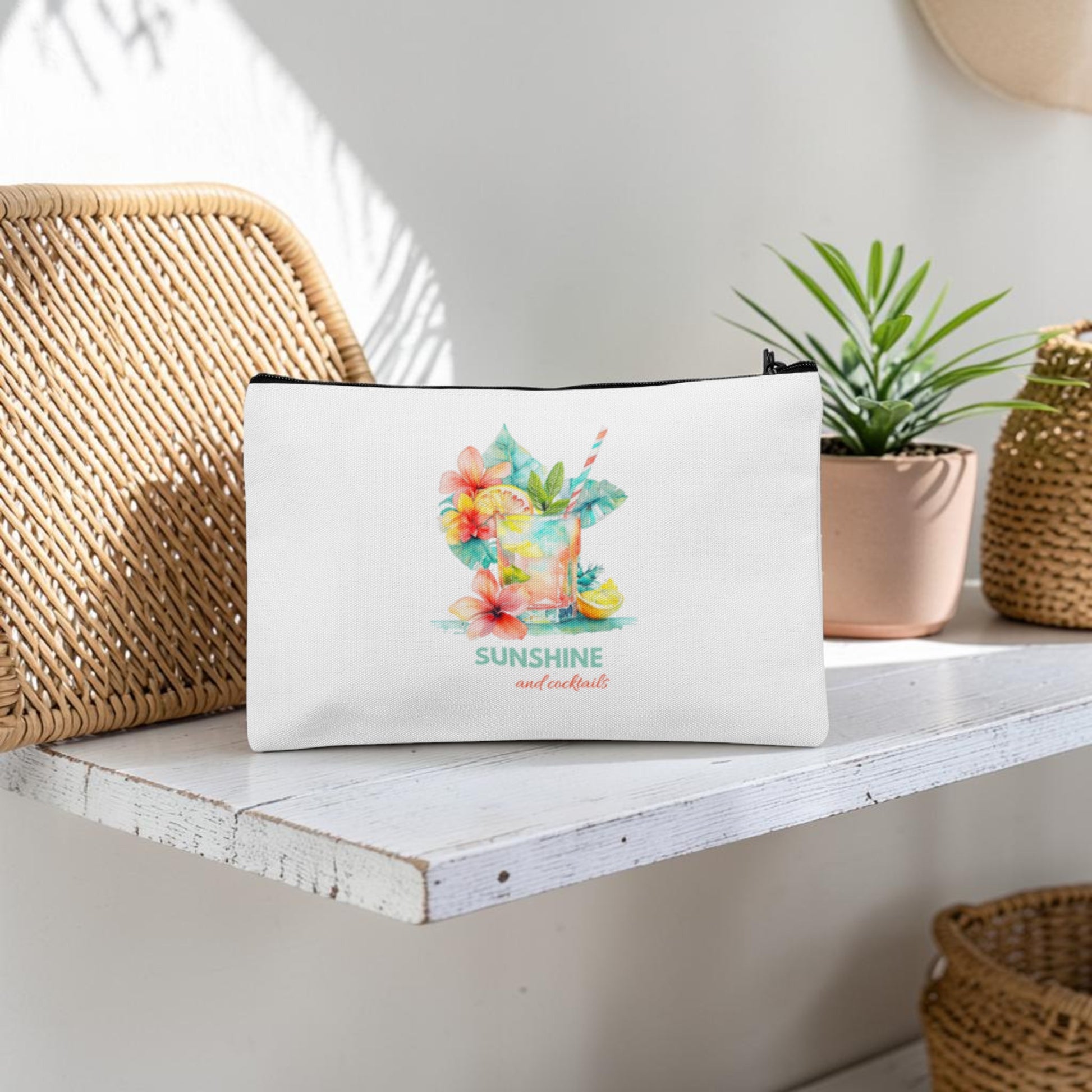The Mirabilia Boutique "Sunshine and Cocktails Makeup Bag," featuring a vibrant tropical drink and floral design with the phrase "Sunshine and cocktails," sits on a white wooden shelf beside a potted plant and woven baskets. Sunlight filters through, casting playful shadows on the wall—making this cheerful travel toiletry pouch the perfect companion for your next getaway.