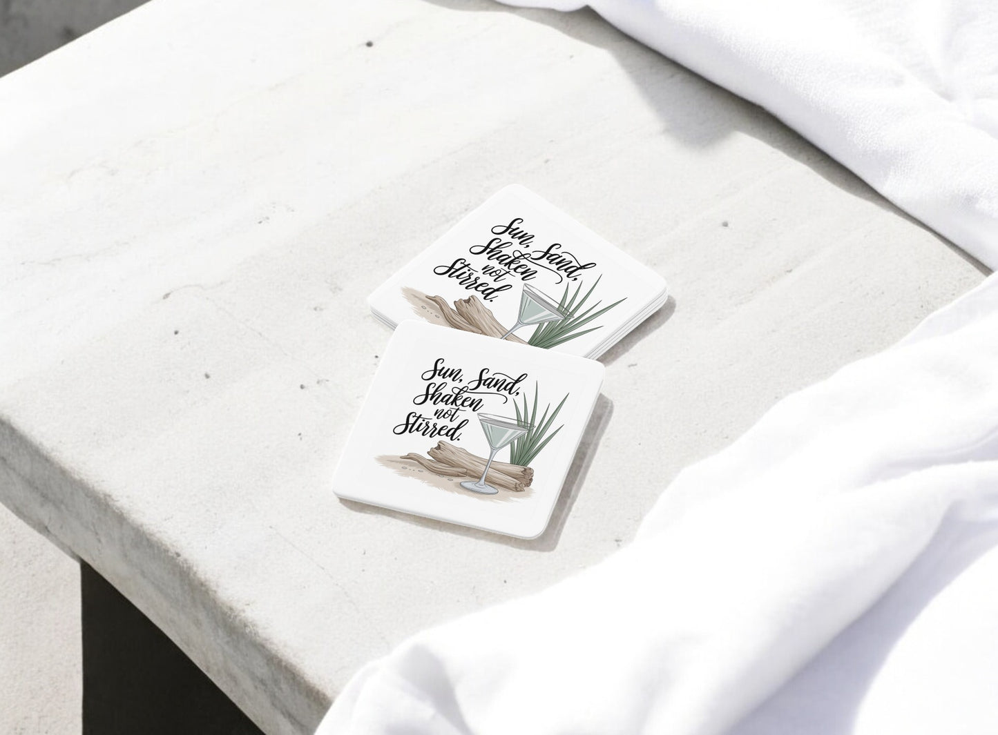 Mirabilia Boutique’s "Sun, Sand, Shaken Not Stirred Coaster Set – Coastal Summer Vibe" features two square coasters adorned with driftwood, green leaves, cocktails, and cursive text—perfect beachy accents for your summer bar cart.