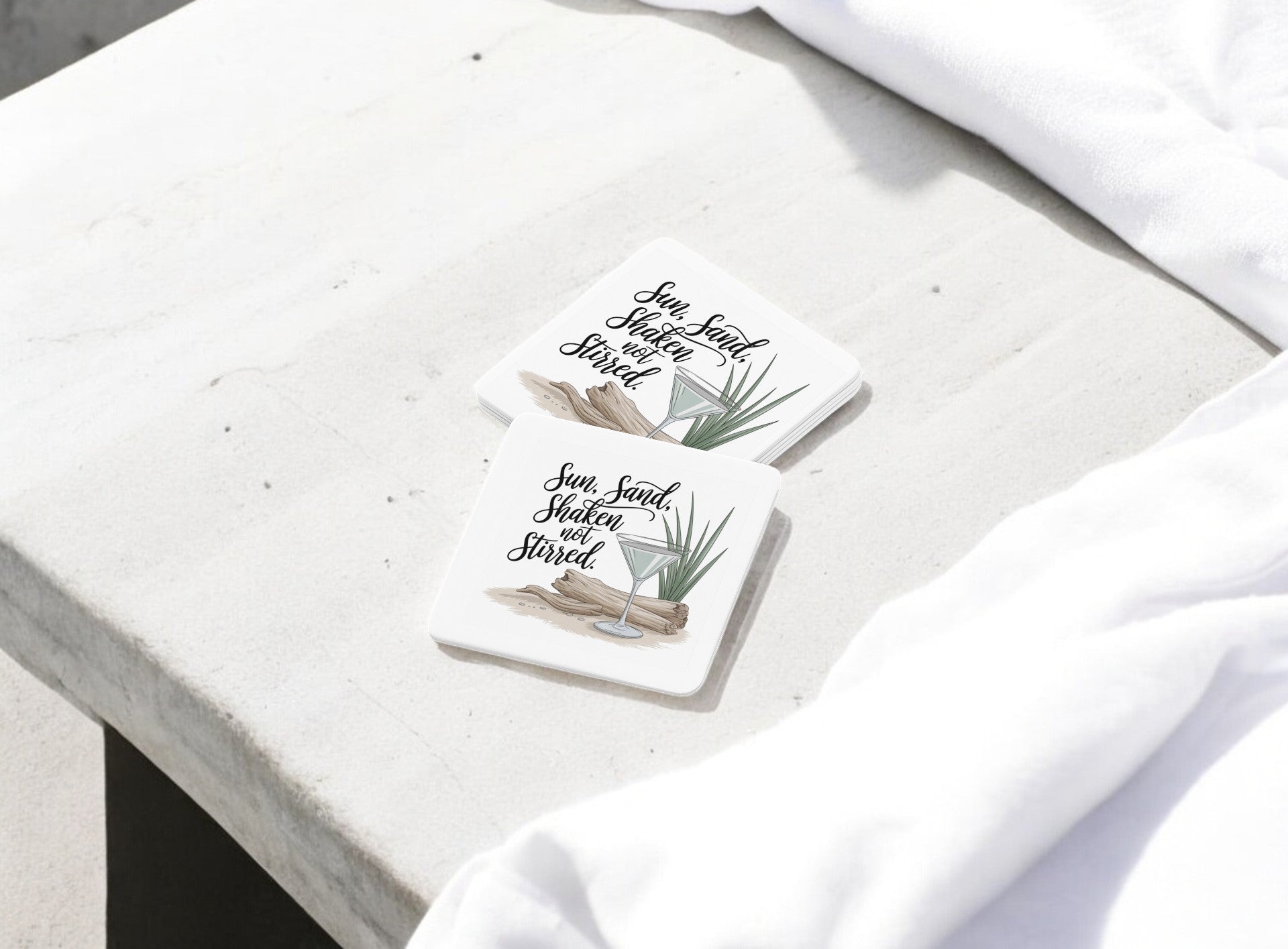 Mirabilia Boutique’s "Sun, Sand, Shaken Not Stirred Coaster Set – Coastal Summer Vibe" features two square coasters adorned with driftwood, green leaves, cocktails, and cursive text—perfect beachy accents for your summer bar cart.