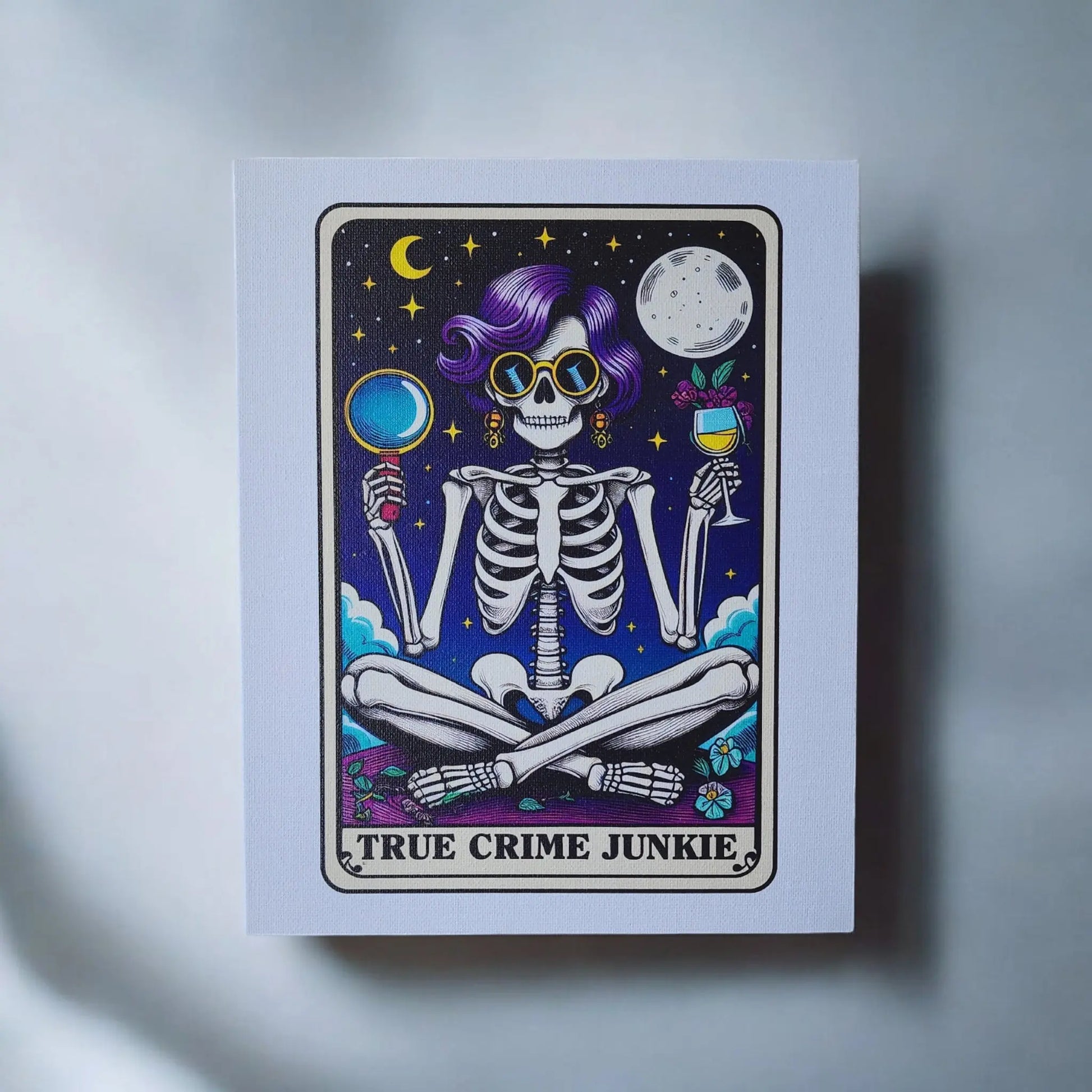 Check out the True Crime Junkie Funny 8x10 Canvas Sign by Mirabilia Boutique! This illustrated canvas print showcases a skeleton with purple hair and sunglasses, sitting cross-legged under a night sky with both crescent and full moons. The skeleton is holding a magnifying glass in one hand and a wine glass in the other. The text at the bottom proudly states "TRUE CRIME JUNKIE." It's the perfect piece of true crime decor!
