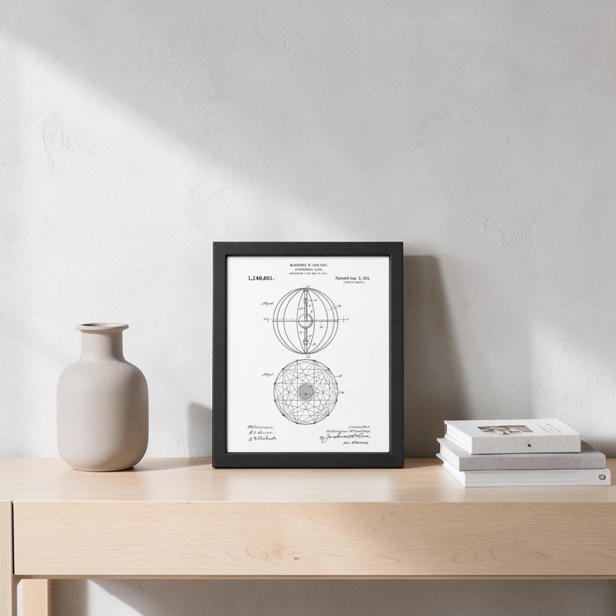 A light wood console table holds a beige ceramic vase, two stacked books, and the Astronomical Globe Patent Art Print by Mirabilia Boutique against a light gray wall with soft shadows.