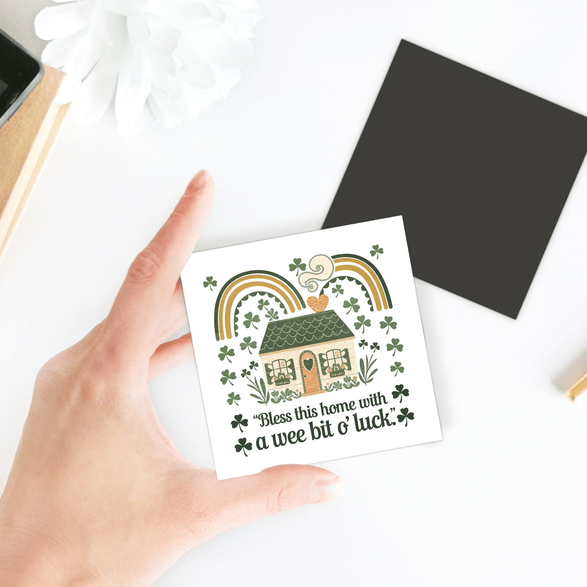 A hand holds the Mirabilia Boutique Wee Bit o’ Luck Irish Home Magnet, featuring an Irish cottage, shamrocks, rainbows, and "Bless this home with a wee bit o' luck!"—perfect as Celtic home decor or a St. Patrick’s Day accent.
