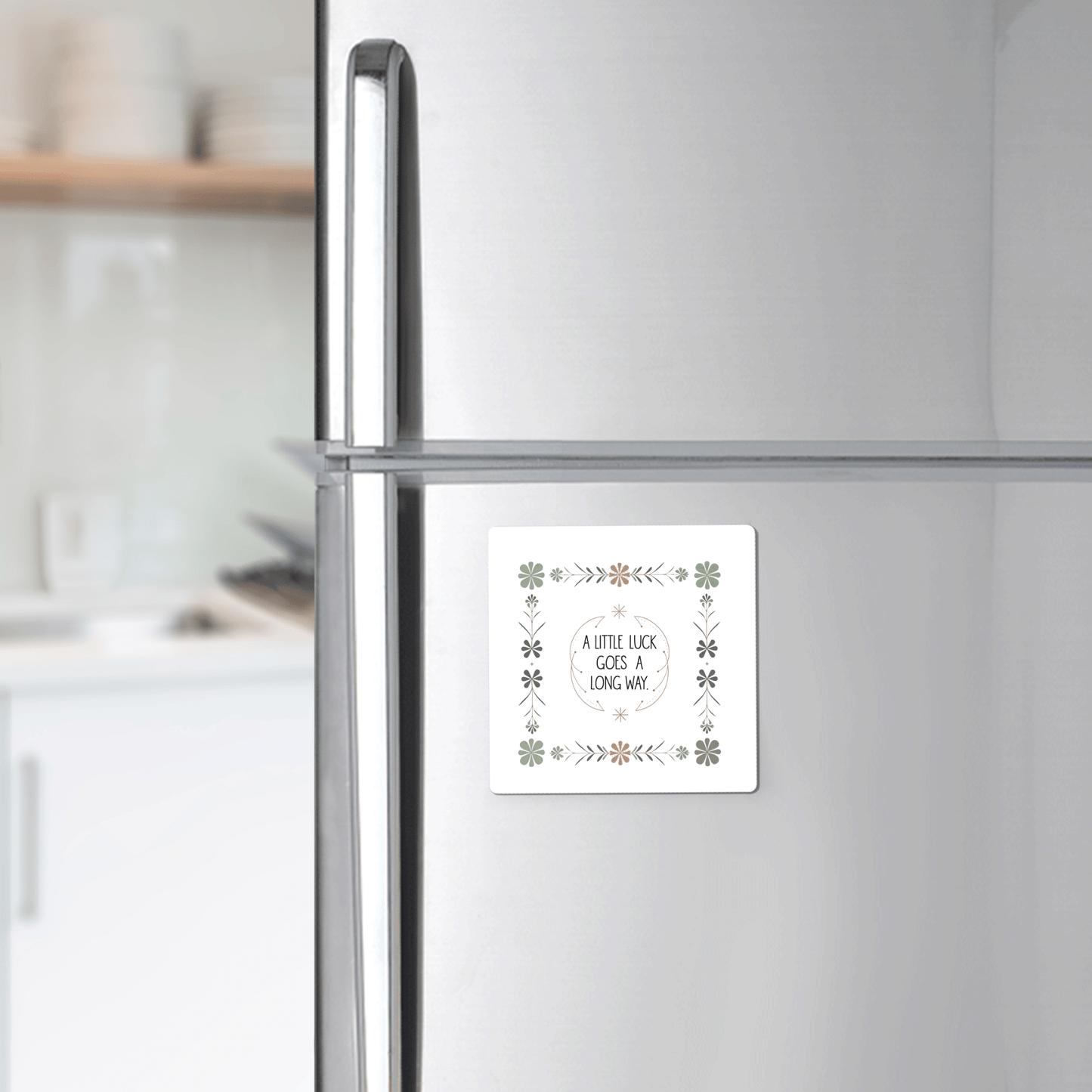 A Mirabilia Boutique "A Little Luck Goes a Long Way" magnet with a green floral border decorates the fridge door, while shelves with dishes appear in the background.