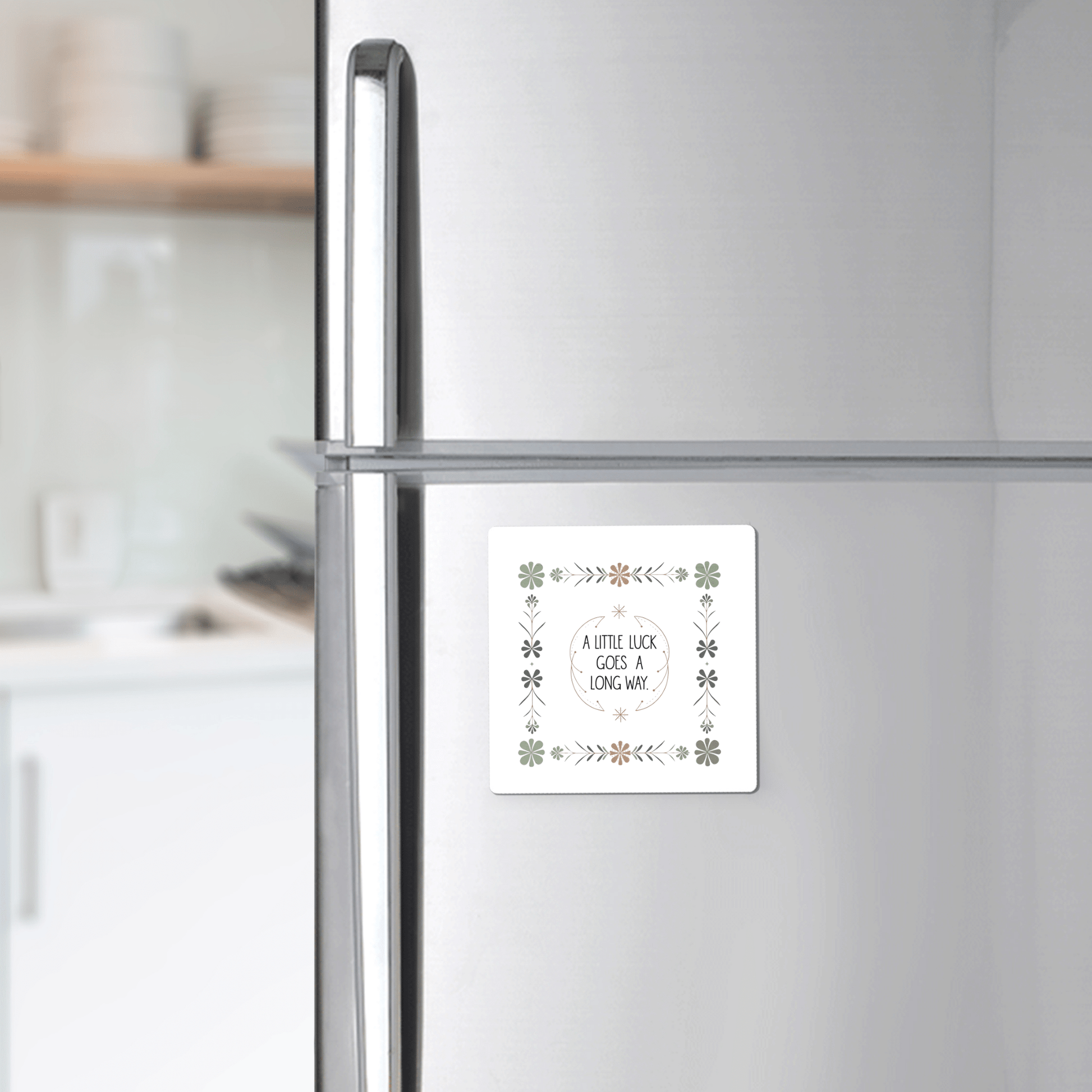 A Mirabilia Boutique "A Little Luck Goes a Long Way" magnet with a green floral border decorates the fridge door, while shelves with dishes appear in the background.