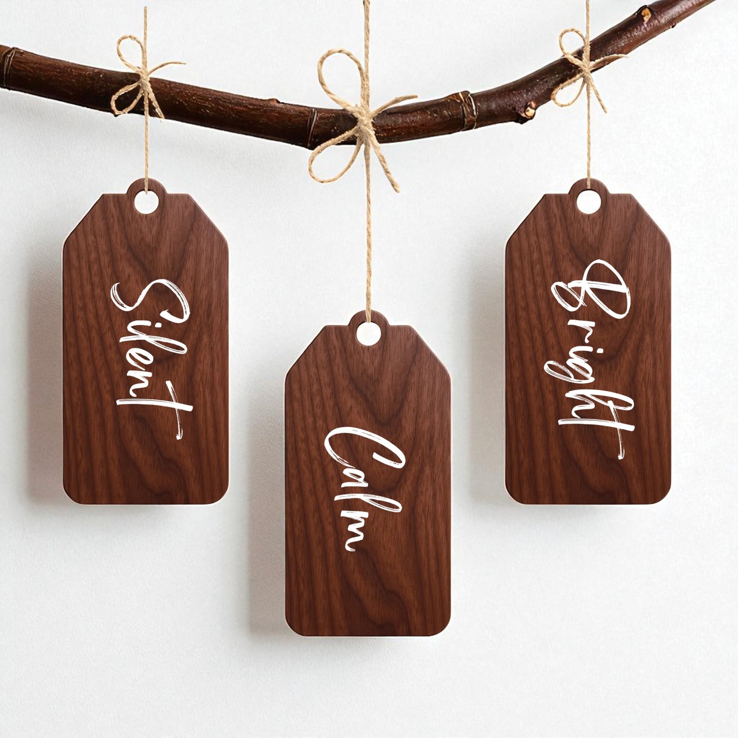 The Walnut Holiday Tags Set by Mirabilia Boutique features three Christmas ornaments—"Silent," "Calm," and "Bright"—crafted from walnut wood and hung with twine bows, adding minimalist holiday style to your decor.