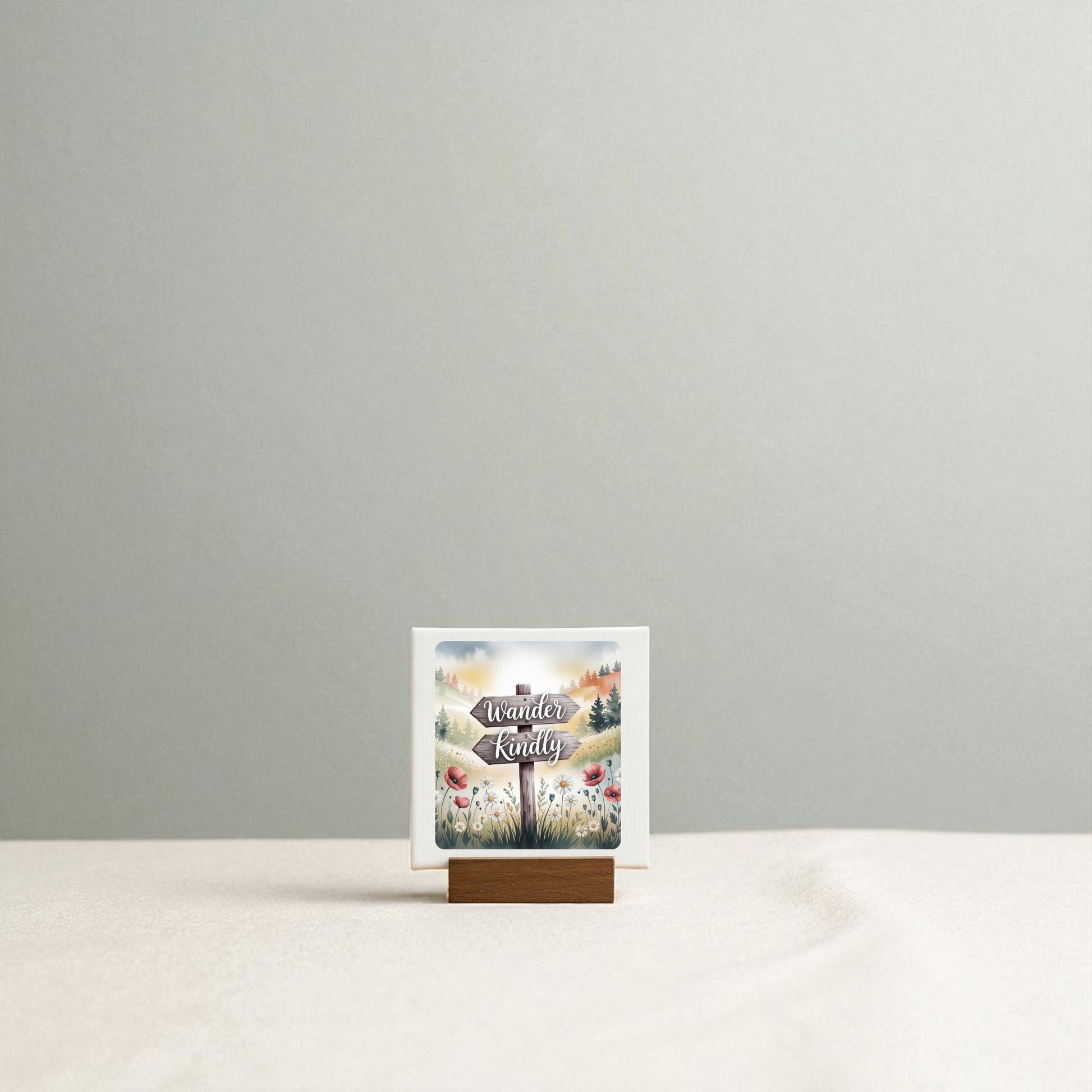 A small card on a wooden stand reads "Wander Kindly" by Mirabilia Boutique, featuring a nature-inspired floral design—perfect mini shelf decor—displayed on a beige surface with a light gray background.