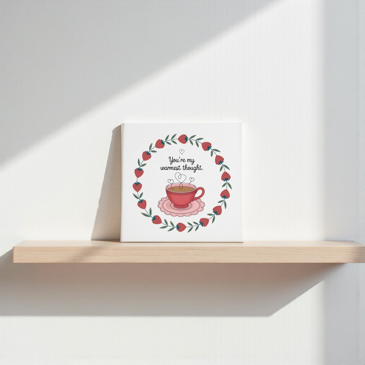 The Warmest Thought Tea-Inspired Canvas Art by Mirabilia Boutique features a red teacup with hearts and a leafy berry wreath, plus “You’re my warmest thought”—a perfect gift for tea lovers or romantic decor.