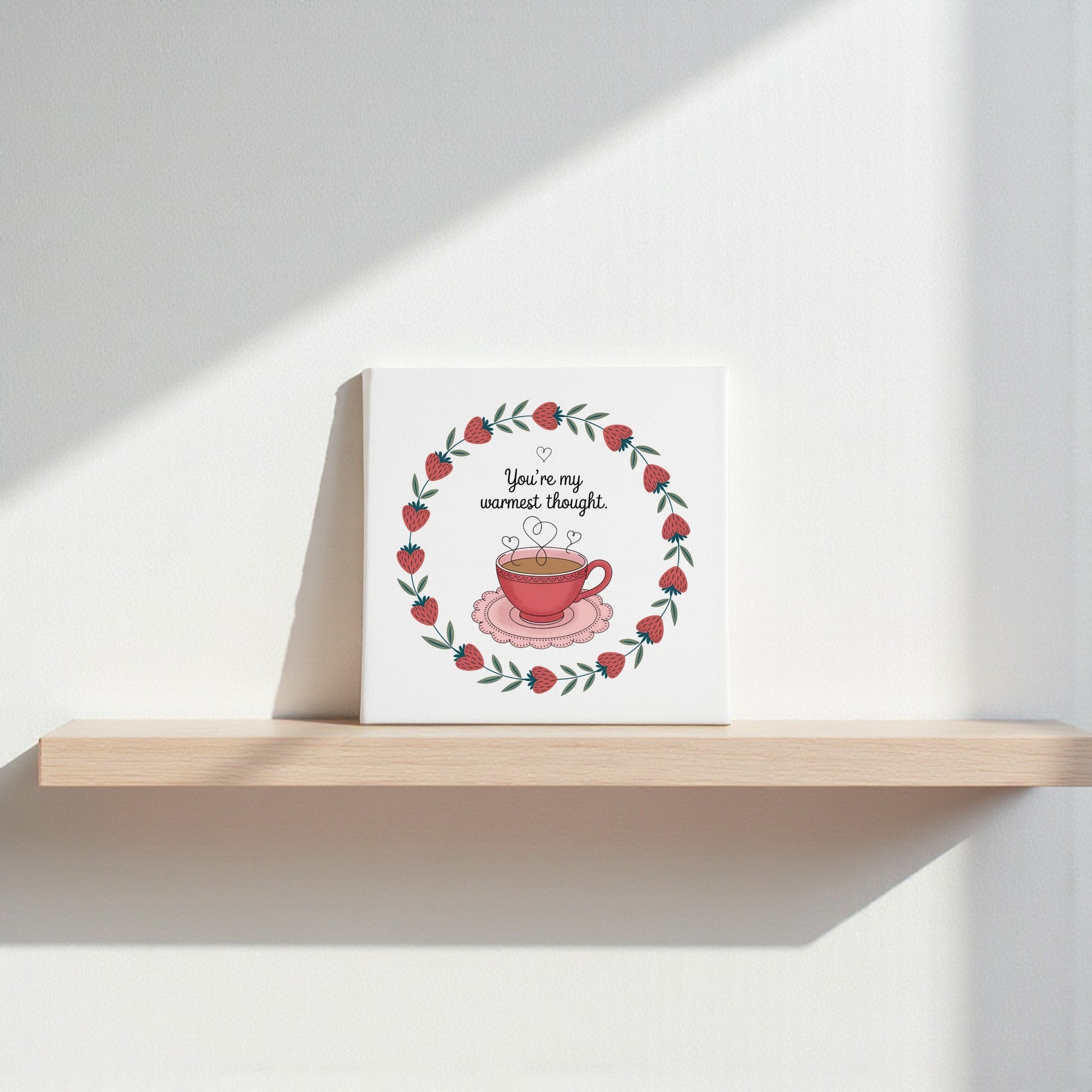 The Warmest Thought Tea-Inspired Canvas Art by Mirabilia Boutique features a red teacup with hearts and a leafy berry wreath, plus “You’re my warmest thought”—a perfect gift for tea lovers or romantic decor.