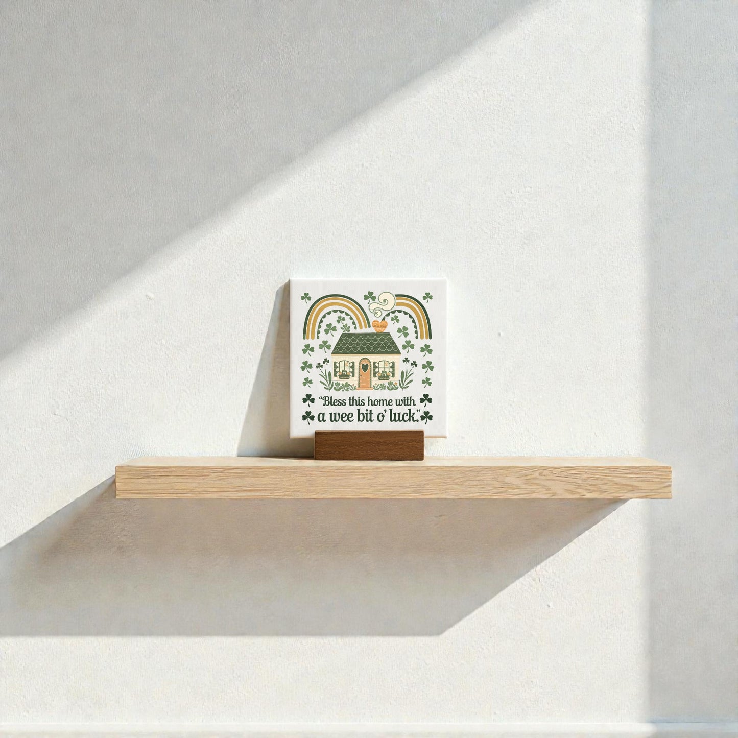 A Wee Bit of Luck Canvas Sign – Irish Cottage Charm by Mirabilia Boutique adds cottagecore flair to a white wall, featuring rainbows, shamrocks, and "Bless this home with a wee bit o' luck" for charming farmhouse decor. Sunlight casts a shadow below.