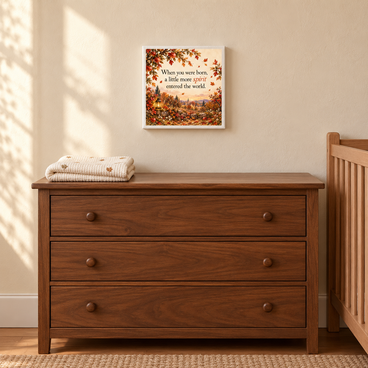 A wooden dresser with folded baby blankets sits beside a crib. Above, the Mirabilia Boutique A Little More Spirit Nursery Keepsake Canvas adds a heartfelt touch to the nursery.
