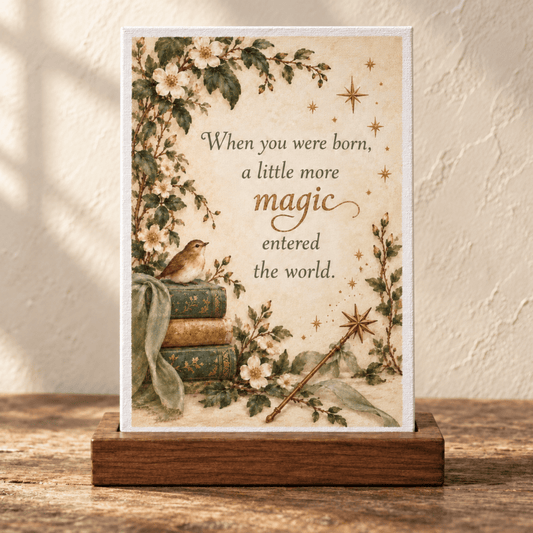 A small rectangular A Little More Magic 4x6 Mini Friend Gift Sign in a wooden stand reading, “When you were born, a little more magic entered the world,” featuring woodland illustrations of books, a bird, flowers, and a magic wand.