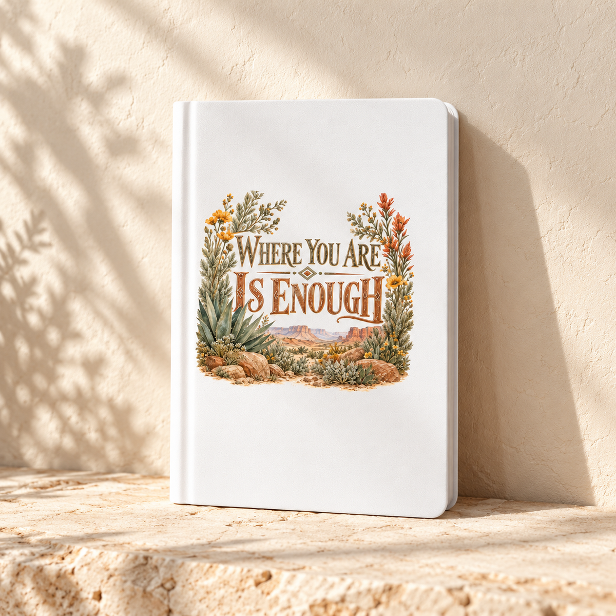 The Where You Are Is Enough A5 Lined Journal | Sage & Stone by Mirabilia Boutique, featuring an inspiring cover with plants and botanicals, sits on stone in natural sunlight.