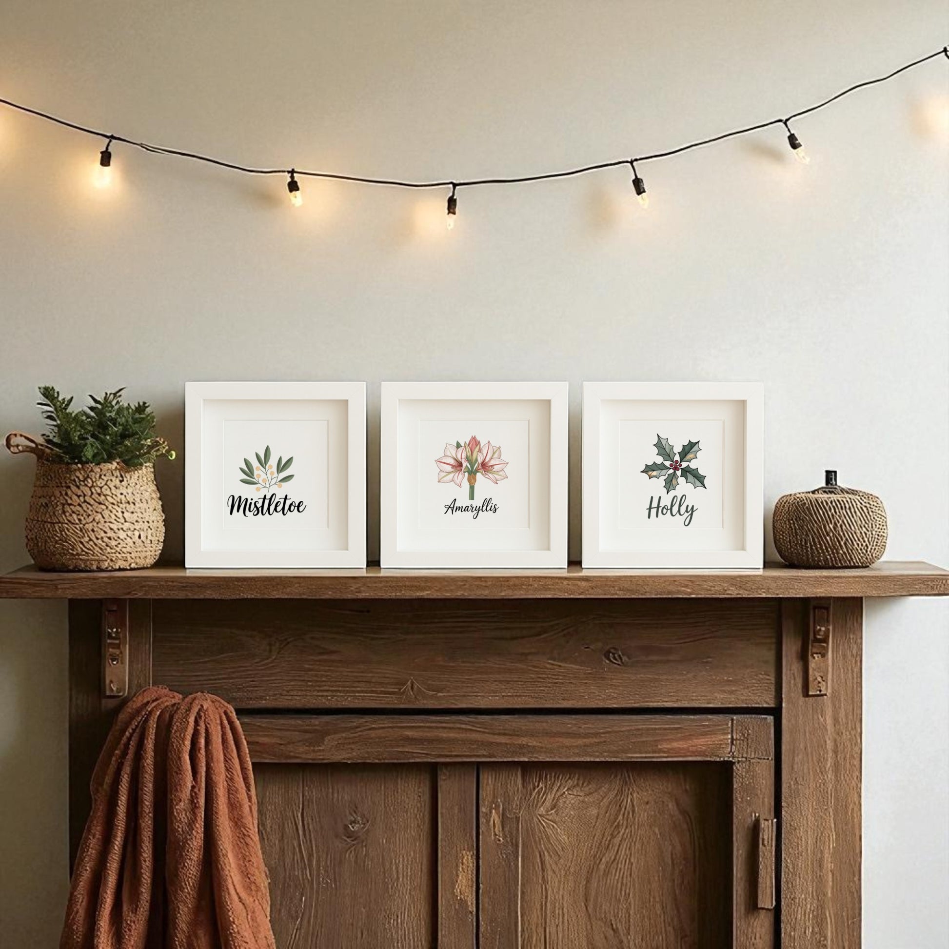 A wooden mantel featuring a knit basket, small plant, and Mirabilia Boutique's "Mistletoe Amaryllis Holly Prints | Holiday Shadowbox Trio," with string lights above, adds festive charm to a neutral wall.