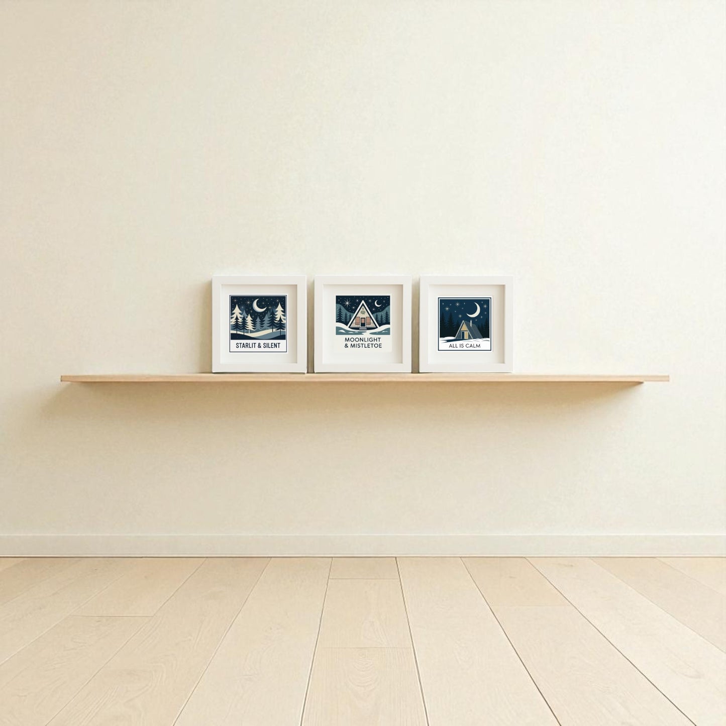 A minimalist room with light wood flooring and cream walls features the Winter Mid-Century Art Trio by Mirabilia Boutique—a floating wooden shelf displays three framed, dark blue and white nature and night sky prints, perfect for cozy holiday wall decor.