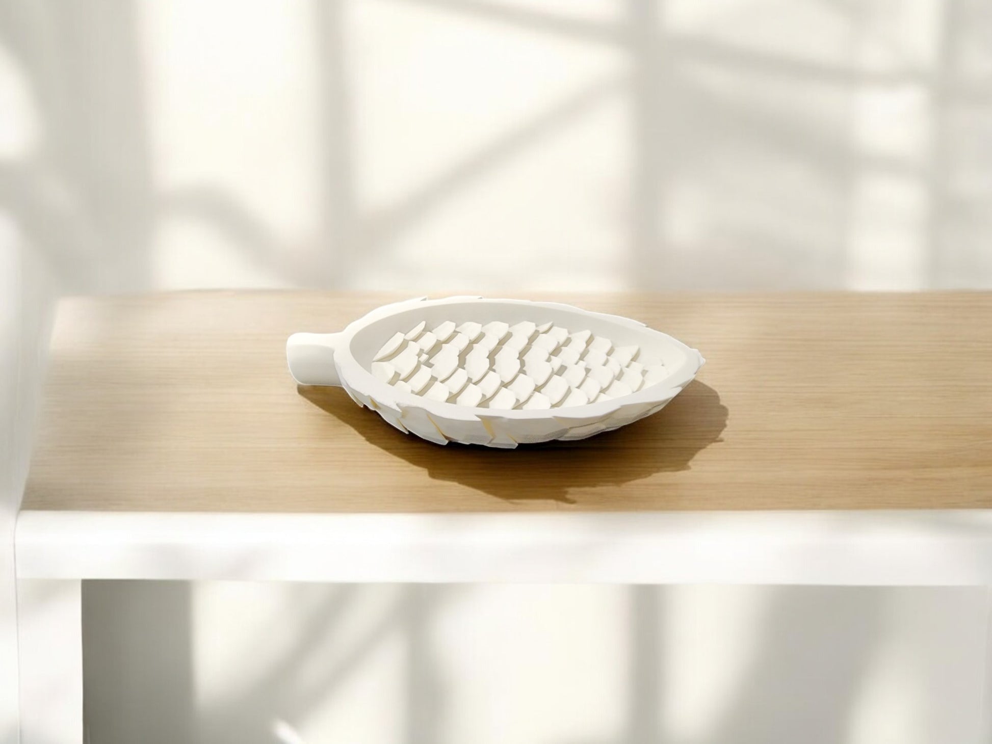 The Mirabilia Boutique Winter White Pinecone Tray sits on light wood, its leaf shape and raised ridges perfect for woodland winter decor, casting soft shadows in the background.