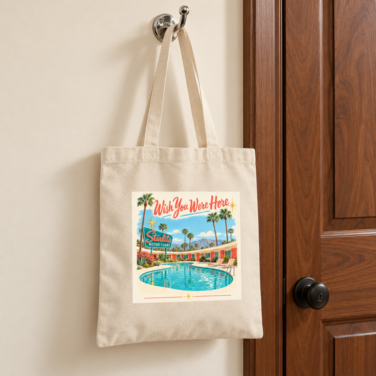 Wish You Were Here Tote | Chrome & Starlight canvas bag hanging on a wall hook, featuring a mid-century postcard illustration of a motel pool with the text “Wish You Were Here” and “Starlite Motor Court.”.