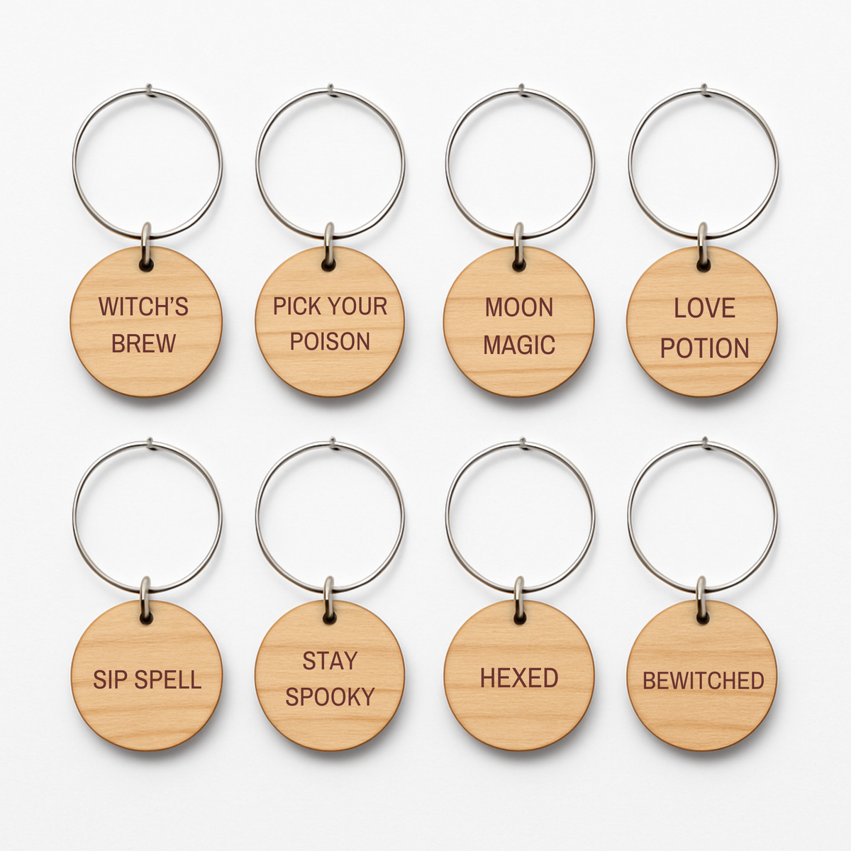 Set of eight Witching Hour Wine Charms by Mirabilia Boutique—round wooden charms with metal rings, each engraved with a distinct Halloween phrase: WITCH’S BREW, PICK YOUR POISON, MOON MAGIC, LOVE POTION, SIP SPELL, STAY SPOOKY, HEXED, and BEWITCHED. Ideal as festive keychains or to enchant your guests as unique wine charms at your next Halloween gathering or for whimsical witchy décor.