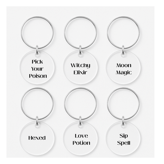 The Witchy Wine Charms Set by Mirabilia Boutique includes six round keychains with silver rings, each with a unique saying, perfect as spooky Halloween drink markers or glass tags for your celebration. White background.