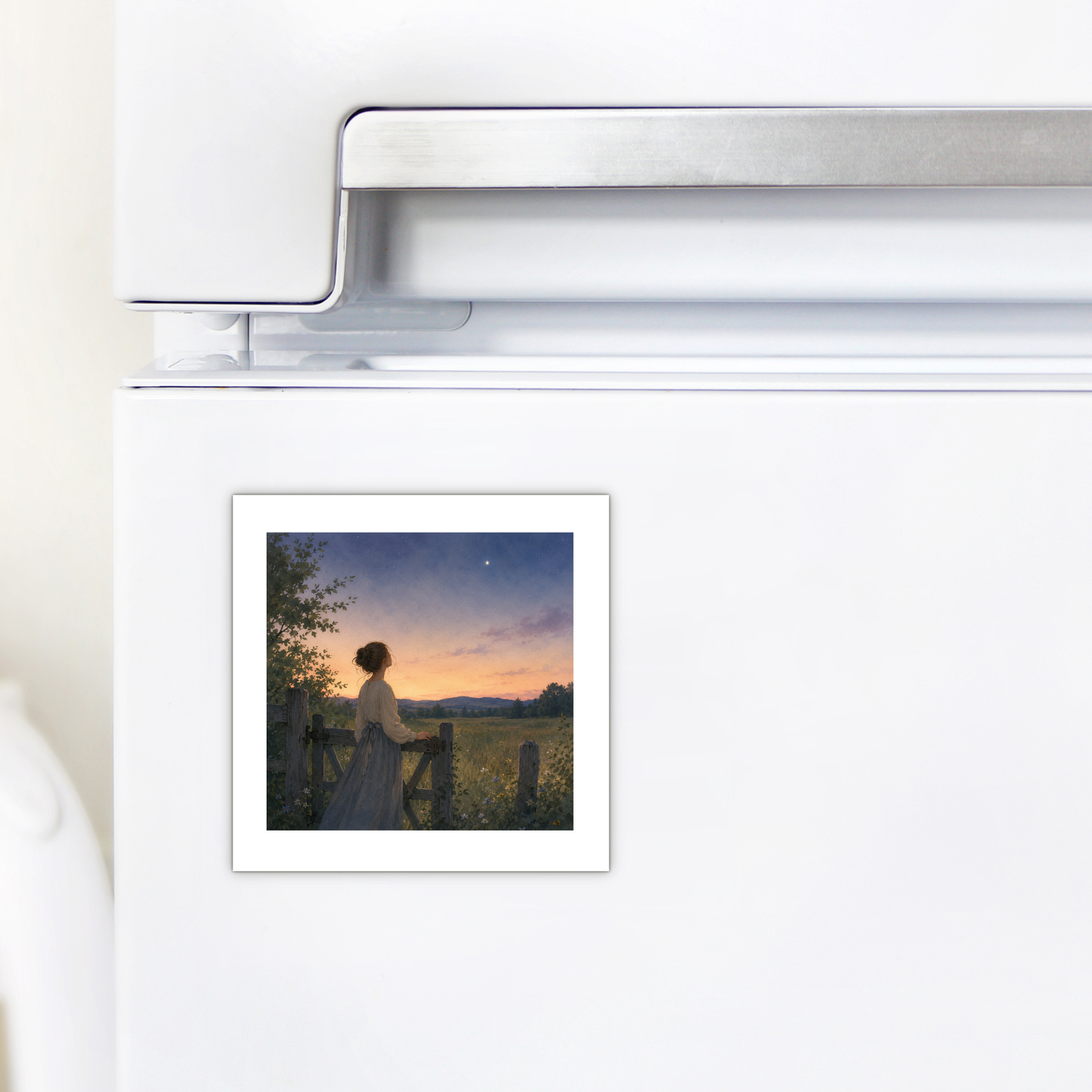 The Wonder, Always Twilight Landscape Magnet | Nature Art from Mirabilia Boutique’s Star & Solstice Collection, showcasing an image of a woman standing by a gate at sunset with a wildflower meadow in the background, is attached to a white refrigerator door.