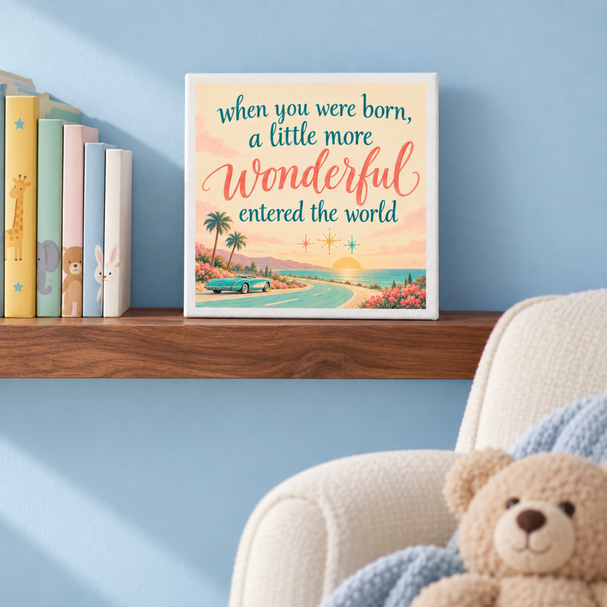 A square When You Were Born A Little More Wonderful Canvas by Mirabilia Boutique featuring a coastal road design sits on a wooden shelf next to children’s books.