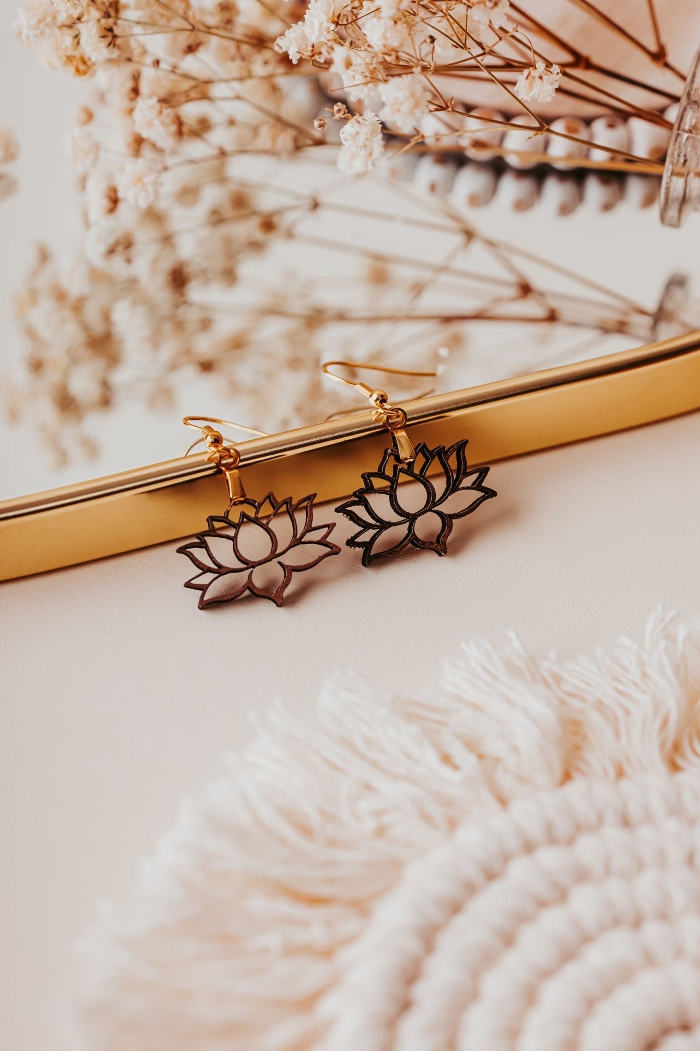Mirabilia Boutique’s Laser Cut Lotus Flower Wood Earrings, lightweight and boho, rest on a mirror with dried flowers, a white woven mat, and natural wood nearby for an elegant, warm touch.