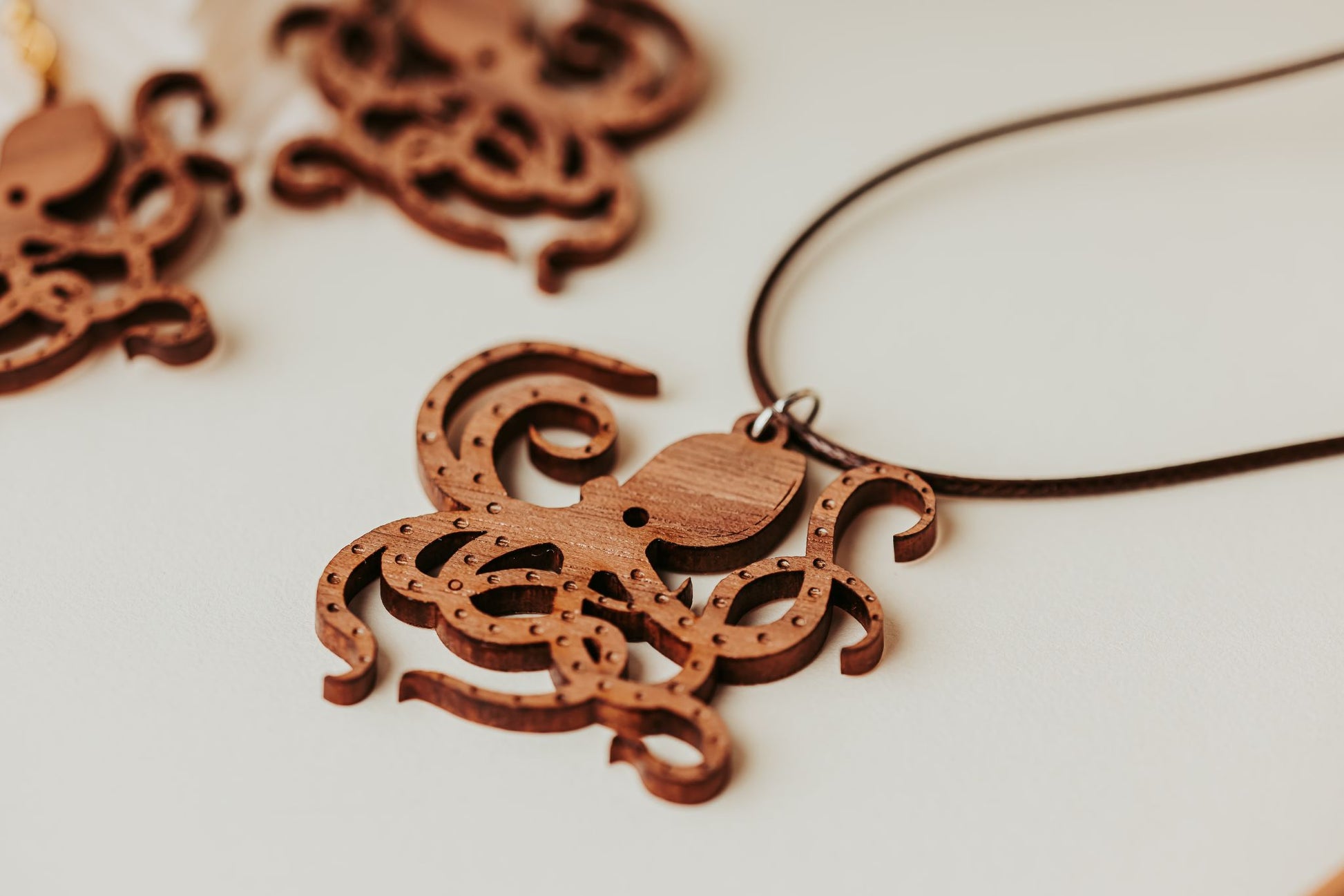 Close-up of the Wooden Octopus Necklace by Mirabilia Boutique, an eco-friendly nautical pendant with intricate cutouts for ocean lovers. The pendant hangs from a dark cord, with another similar design softly blurred behind.