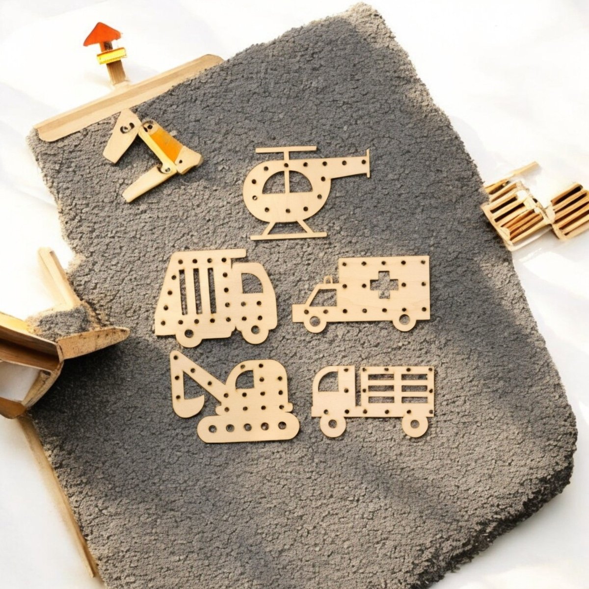 Mirabilia Boutique's Vehicle Lacing Trays for Fine Motor Skills feature wooden helicopter, bus, ambulance, excavator, and truck shapes—ideal for preschoolers to learn and practice motor skills on a textured gray surface.