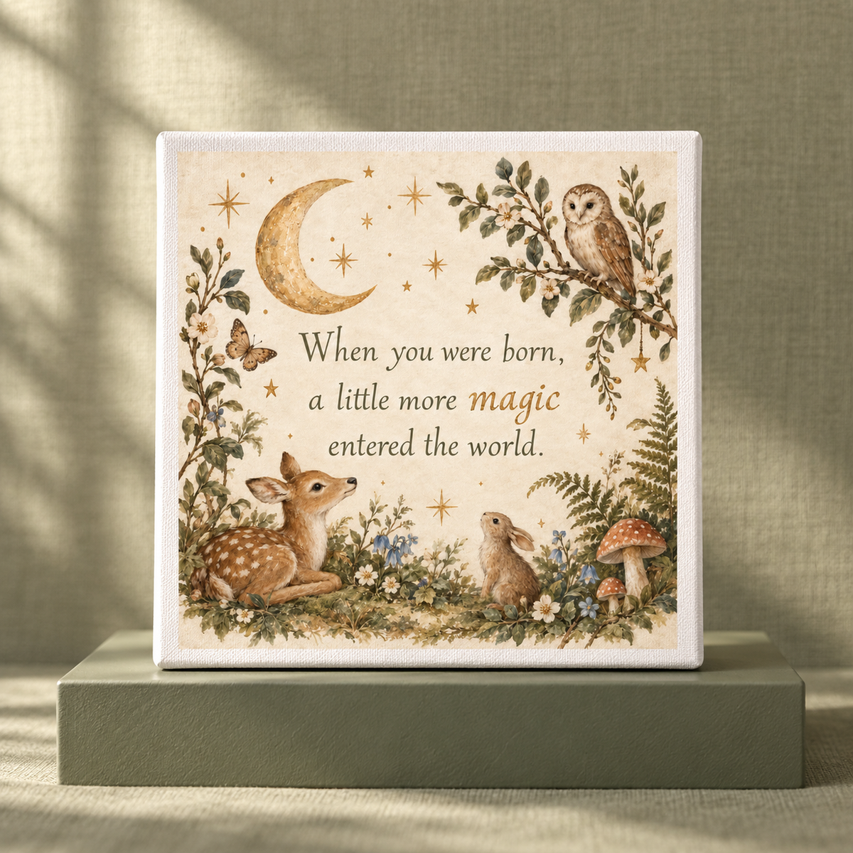 The Mirabilia Boutique “A Little More Magic” 8x8 Woodland Nursery Canvas features a moon, owl, fawn, and rabbit nestled among plants on a soft green background. Adorned with the heartfelt text, “When you were born, a little more magic entered the world,” this charming canvas from Mirabilia Baby makes a cherished keepsake for any nursery.