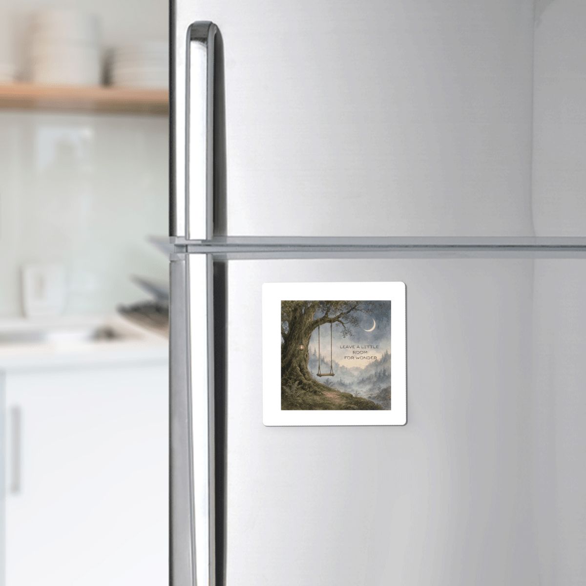 A silver fridge adorned with the "Leave a Little Room for Wonder" magnet from Mirabilia Boutique, featuring a fantasy forest scene with a swing and an inspiring quote, adds charming nature-themed décor to a white kitchen.