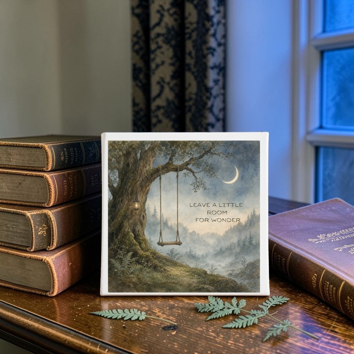 The Leave a Little Room for Wonder Canvas by Mirabilia Boutique is a nature-inspired décor piece showcasing a tree with a swing and a crescent moon, along with the quote "Leave a little room for wonder." Displayed on a wooden table beside vintage books, fern leaves, and near a window, it brings woodland charm to any space.
