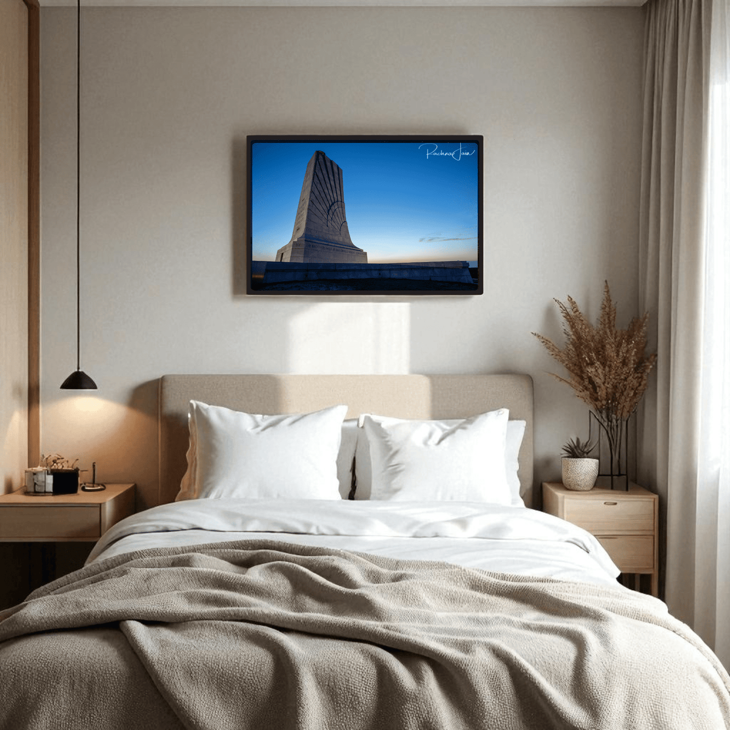 A cozy bedroom features a neatly made bed, two bedside tables with lamps, a vase of dried plants, and the Mirabilia Boutique Wright Brothers Monument Print | First in Flight Wall Art hanging above the bed.