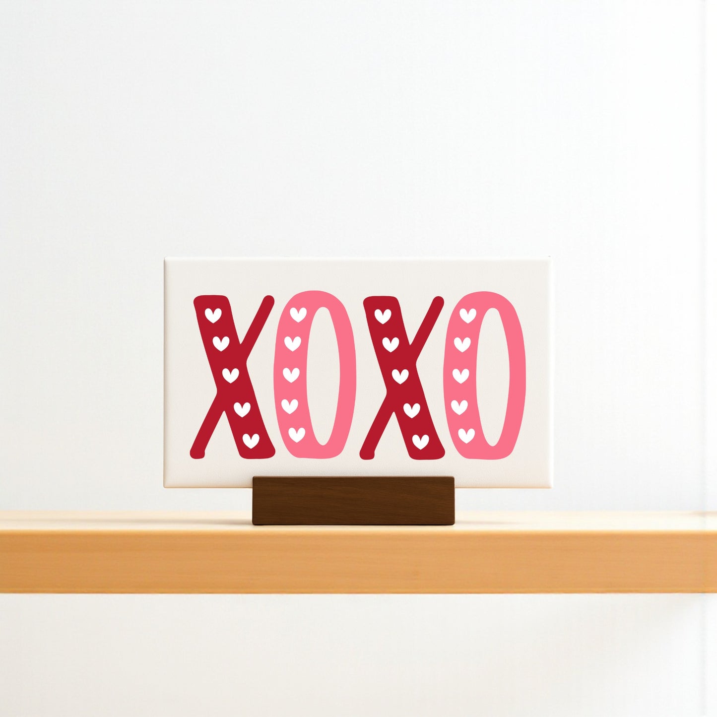 The Mirabilia Boutique XOXO Valentine's Sign is a 6x4 canvas with a wood base, featuring bold red and pink letters with tiny white hearts—ideal Valentine’s Day decor.
